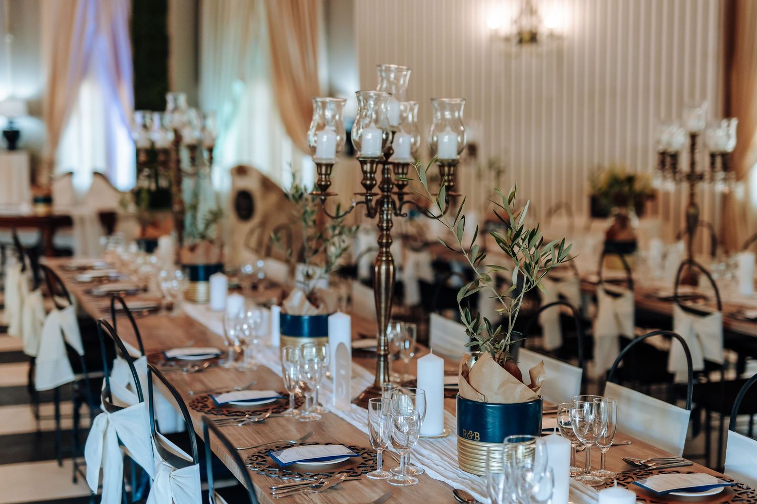 Elegant wedding reception table setting with crystal candelabras, navy accents, and greenery centerpieces in a ballroom.