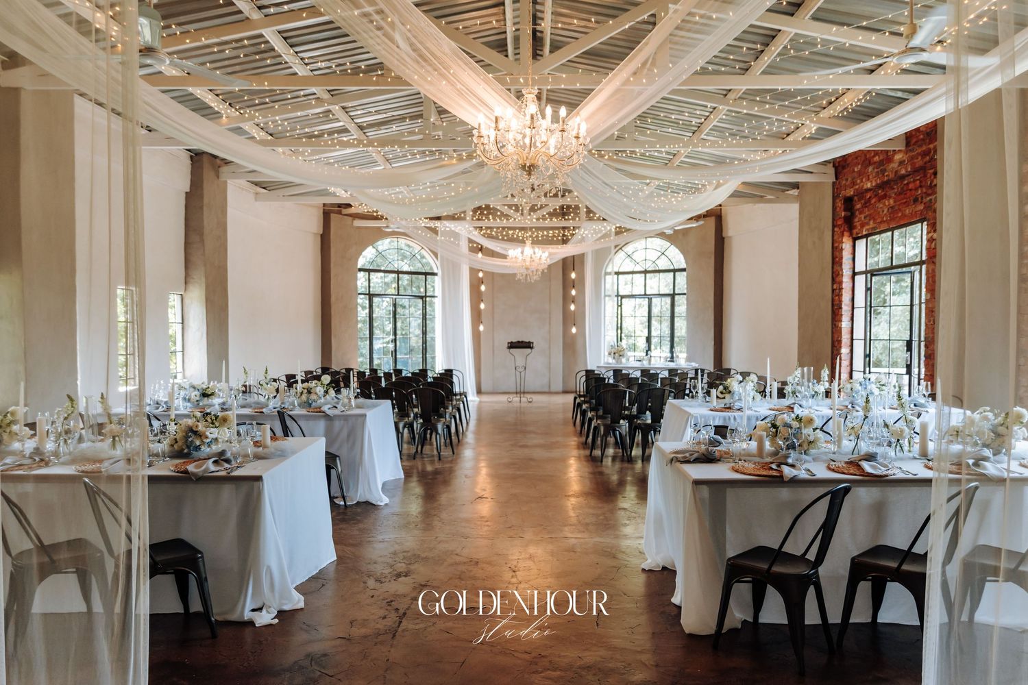 Elegant wedding venue interior with crystal chandeliers, white decor, and natural light streaming through large windows.