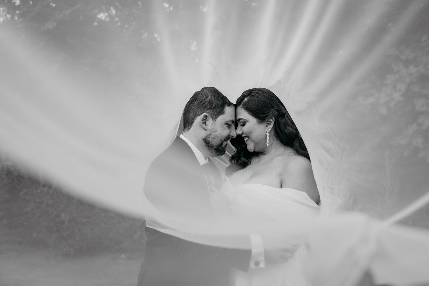 A couple in wedding attire shares a romantic kiss under a white veil during their wedding ceremony.