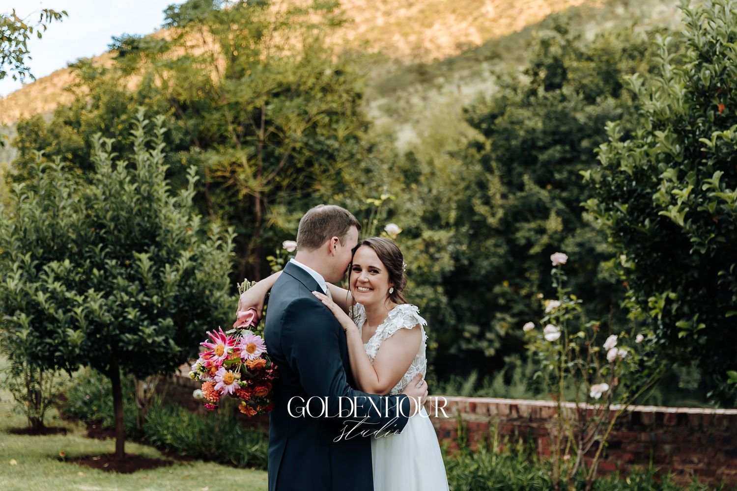 Bride and groom share a romantic embrace in a lush garden with colorful bouquet.