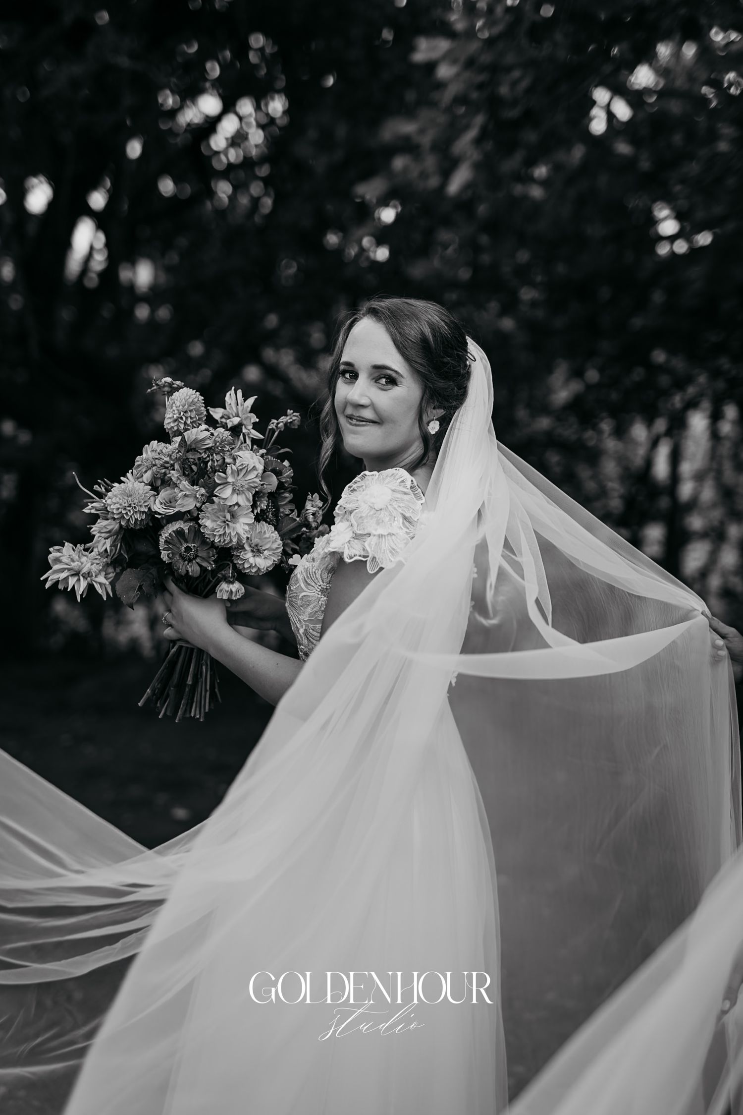 Black and white portrait of bride holding bouquet with flowing veil caught in the breeze outdoors.