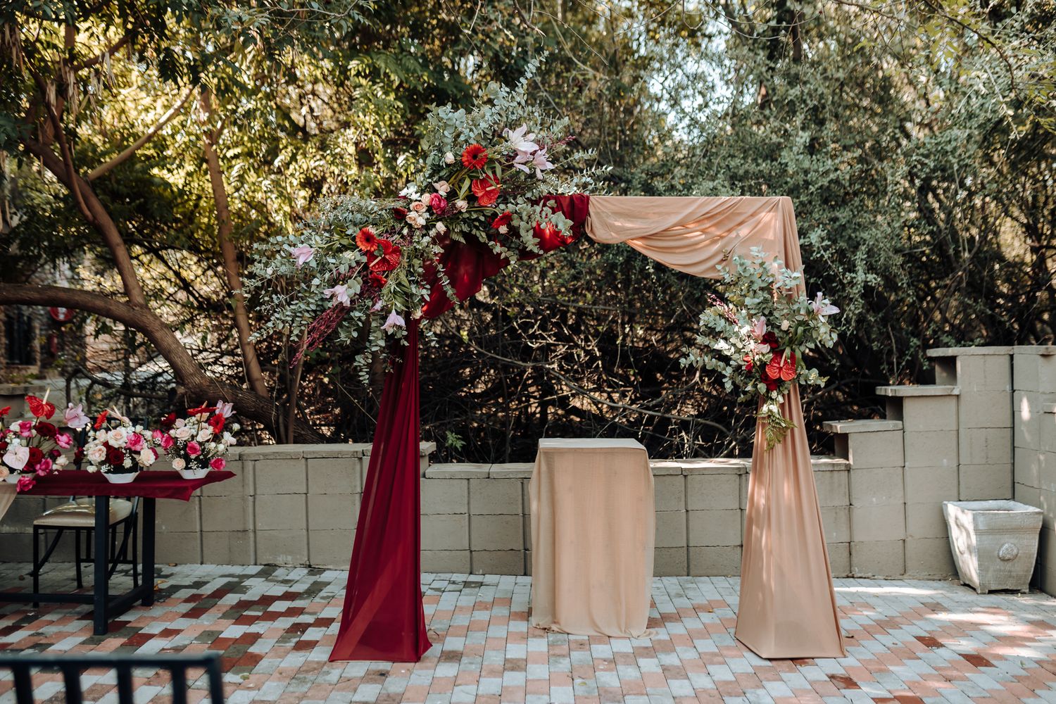 Elegant wedding arch with burgundy and pink floral arrangements against a garden backdrop.