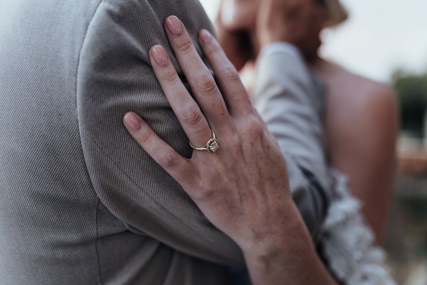 Close-up of an elegant engagement ring on hand resting against a grey suit jacket.