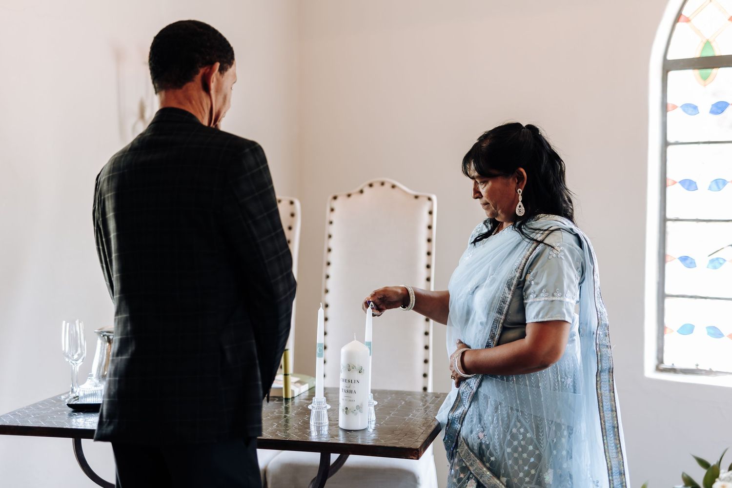 Two people preparing for a ceremony at a table with a lighted mirror in the background.