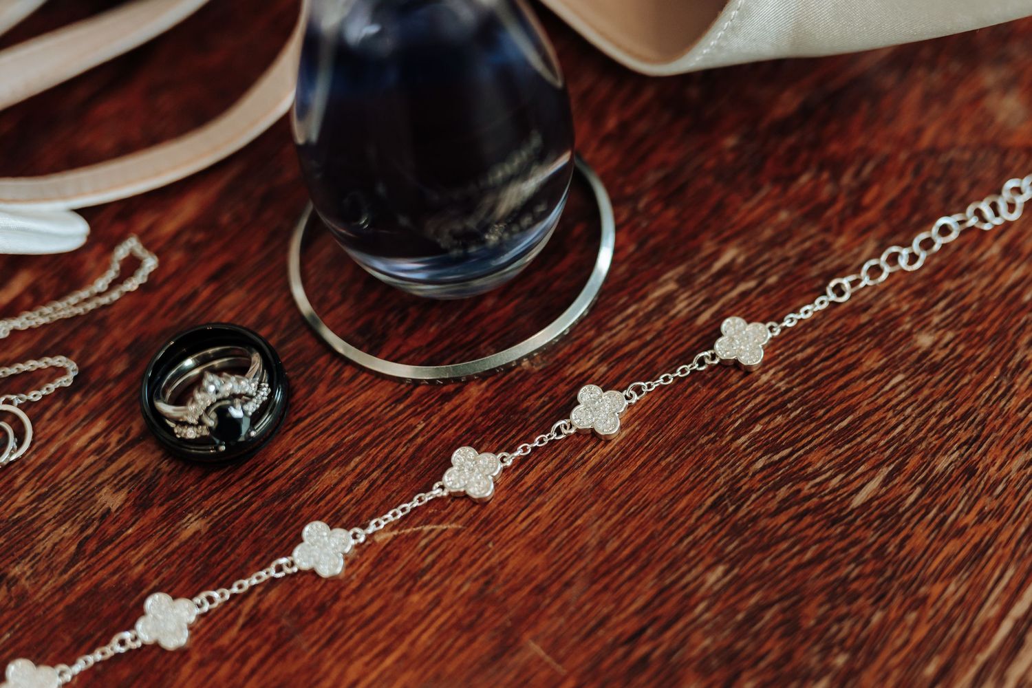 Wedding jewelry and accessories artfully arranged on rich wooden surface with glass bottle detail.