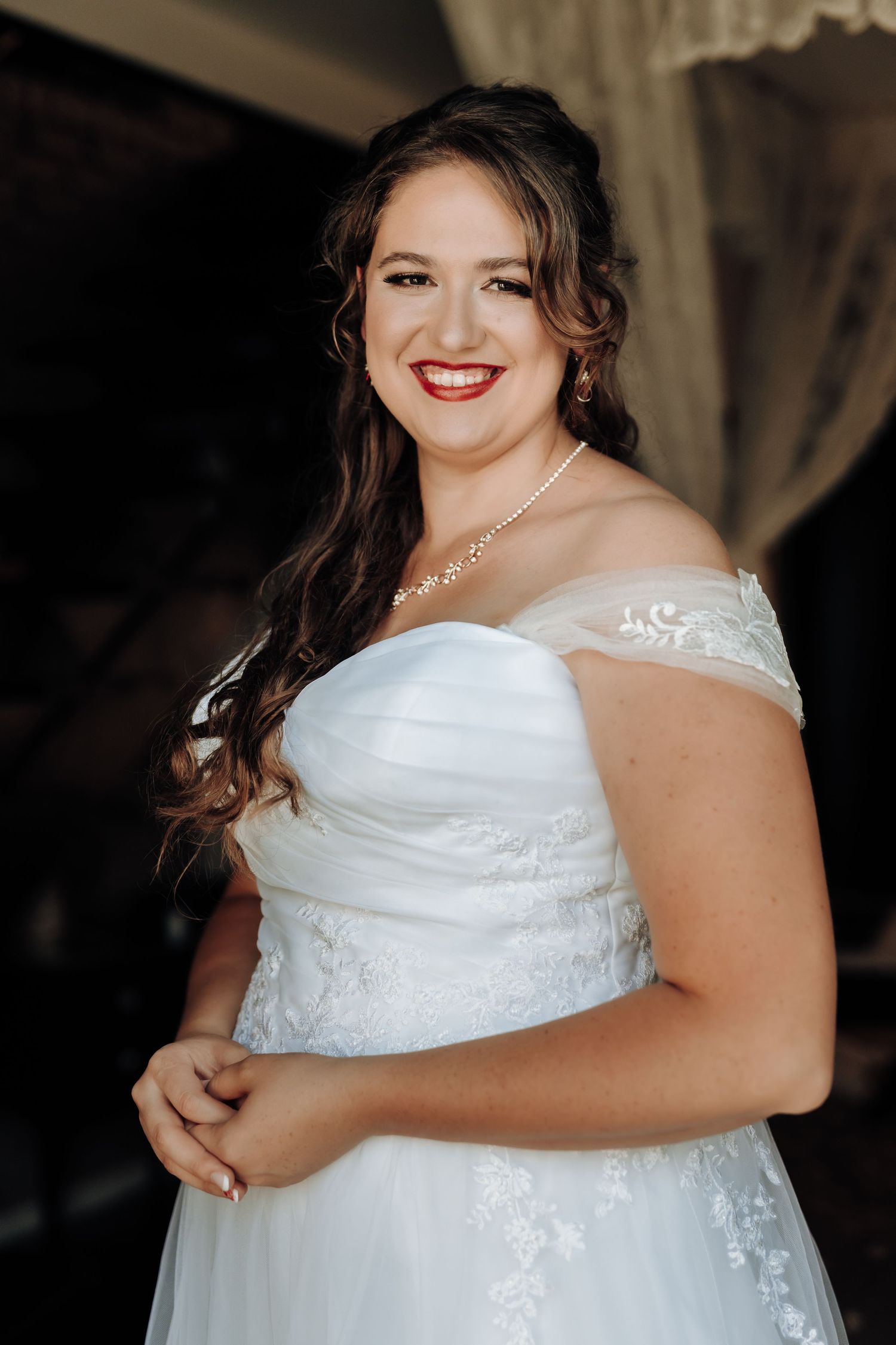 Elegant bride in off-shoulder gown smiles radiantly in wedding portrait.