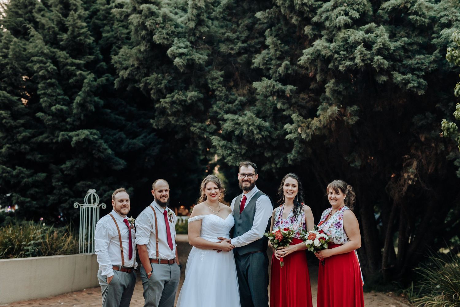 Wedding party poses against evergreen backdrop with red and grey color scheme.