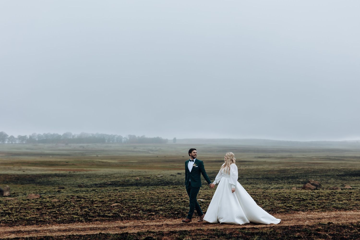 A wedding couple poses together against a misty landscape and dramatic cloudy sky.