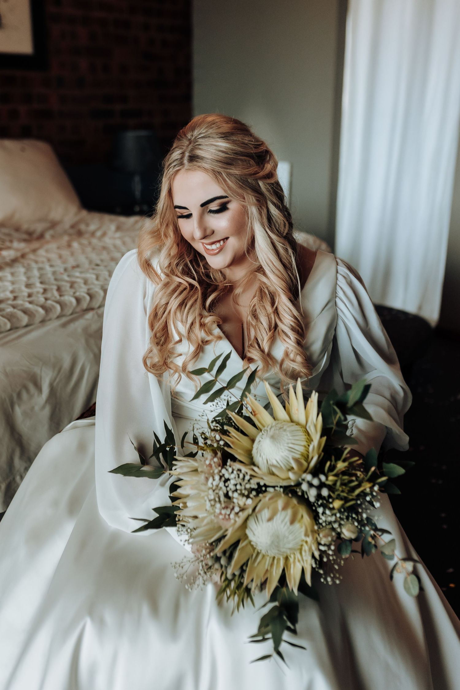 Bride in white wedding gown holding unique dried flower bouquet with natural sunflowers.