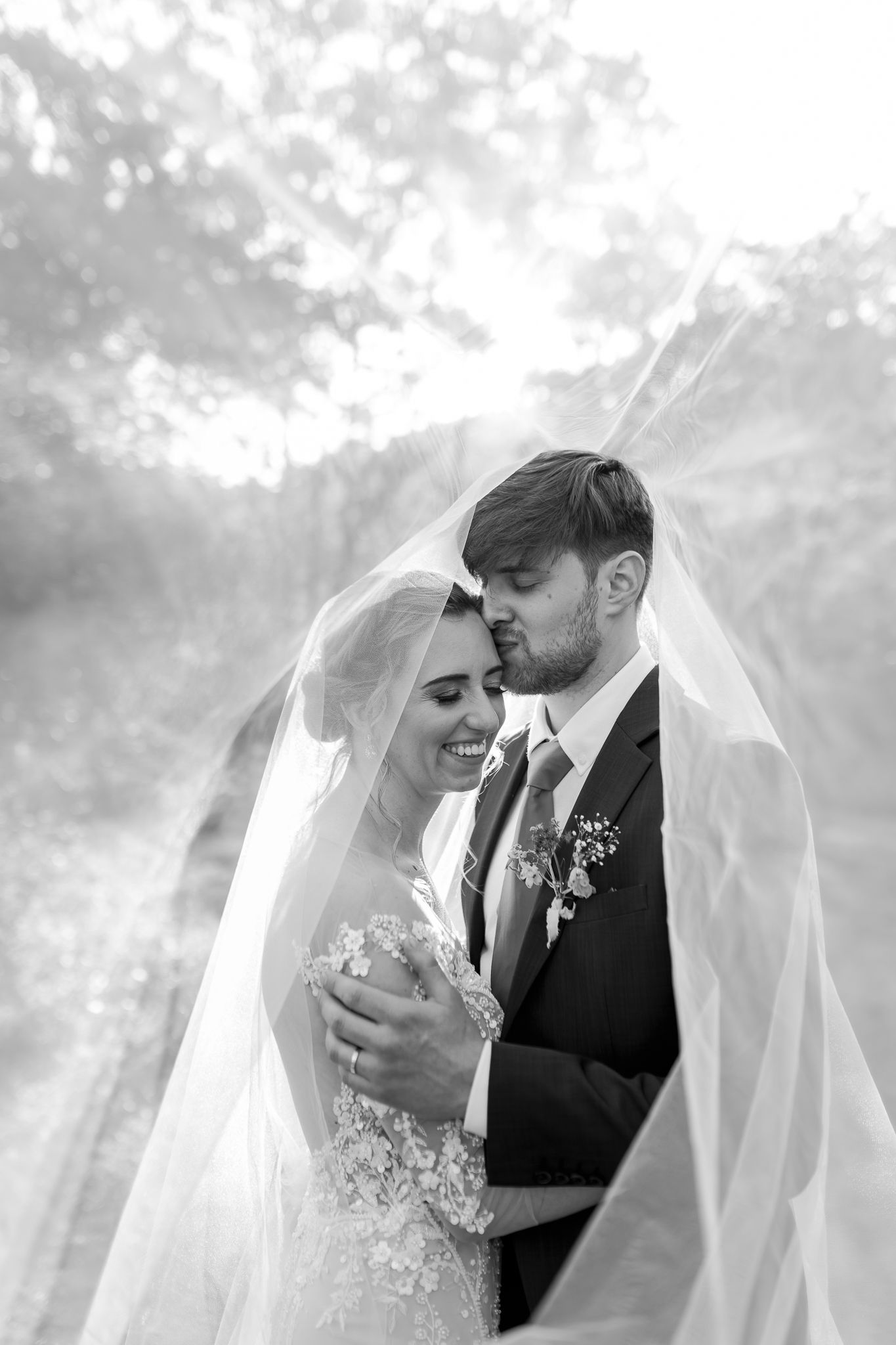 Intimate black and white wedding portrait with couple sharing a tender moment under flowing veil.
