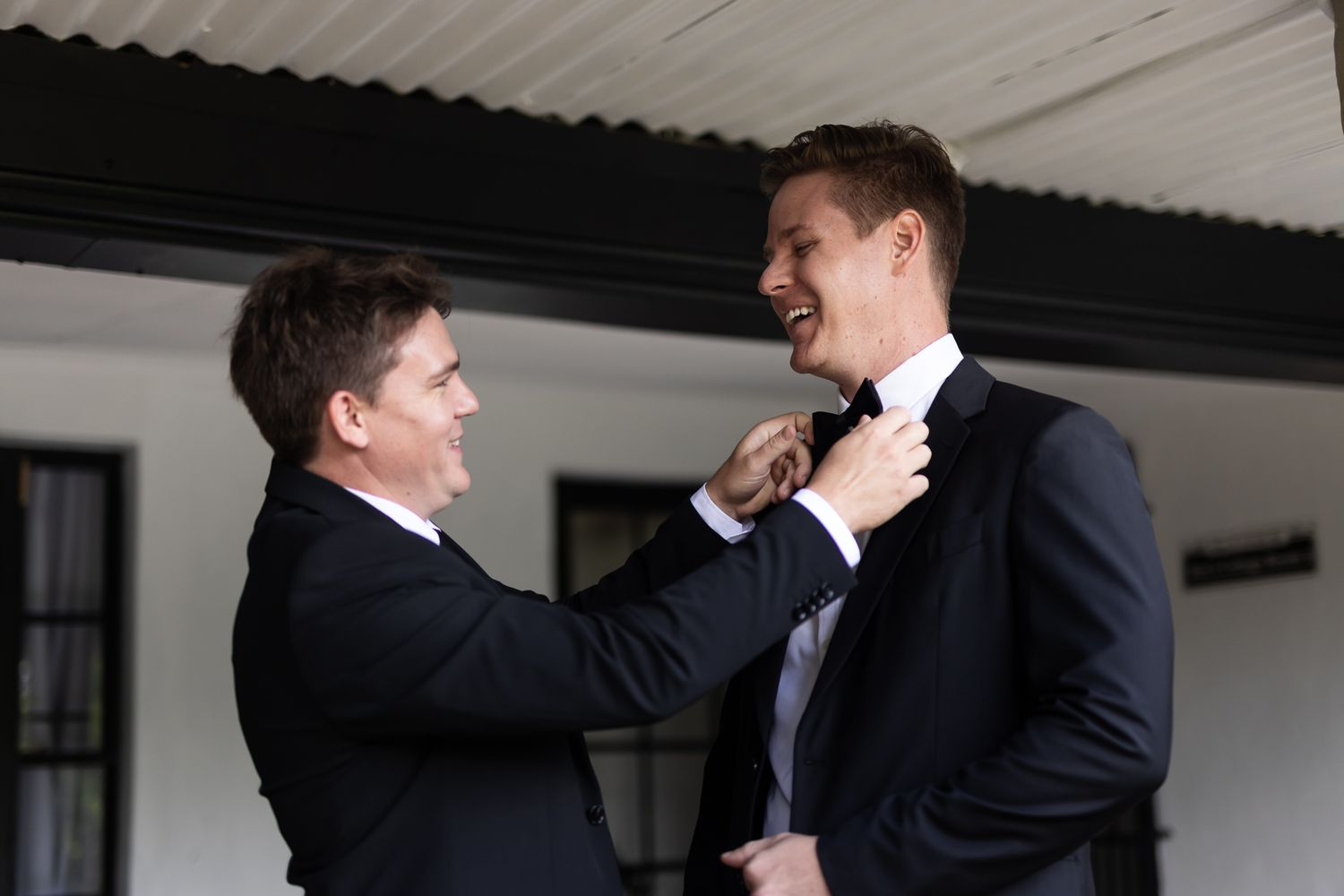 Two people in formal wear helping each other adjust neckties and clothing.