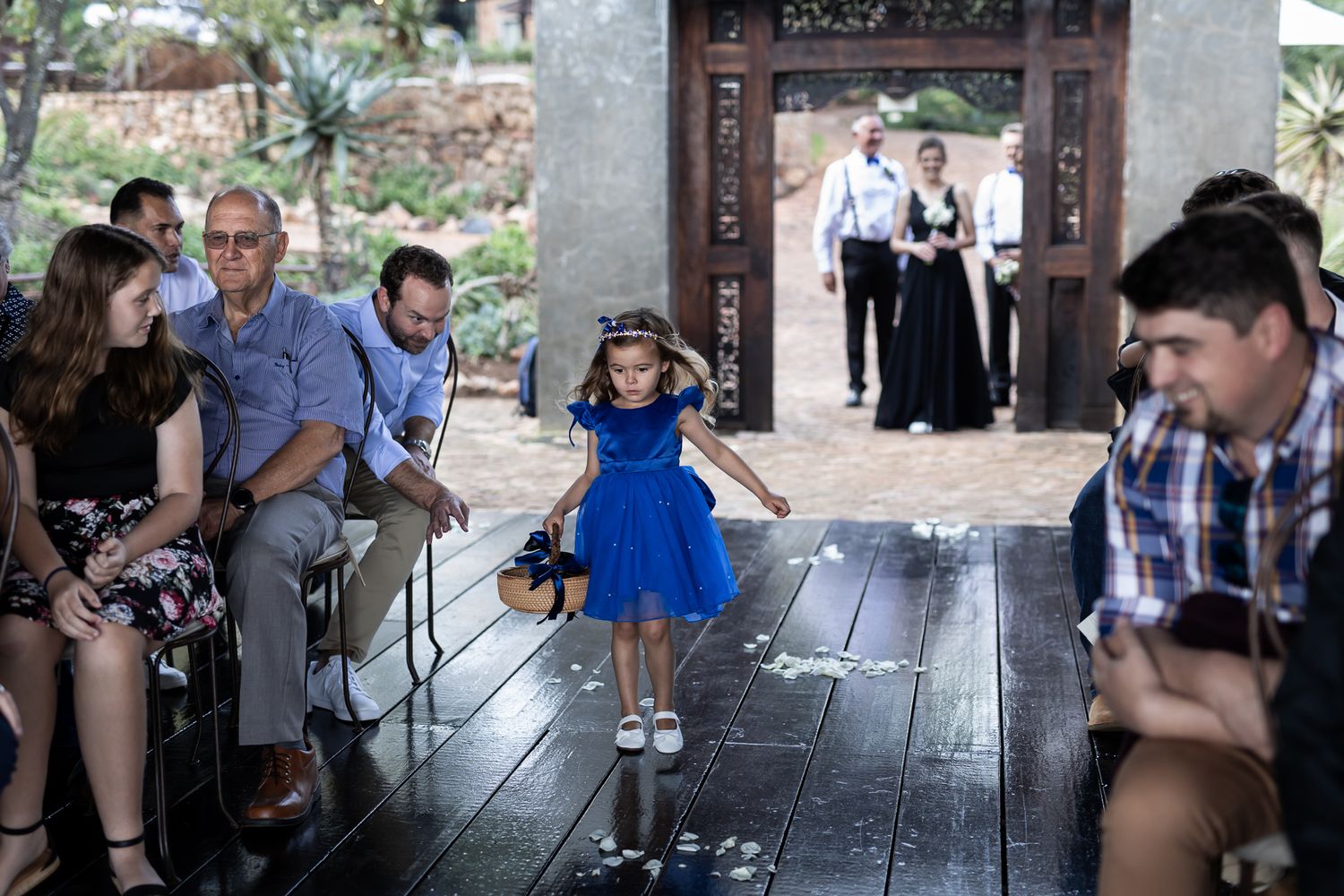 Small child in blue dress twirls on wooden deck during outdoor wedding ceremony.
