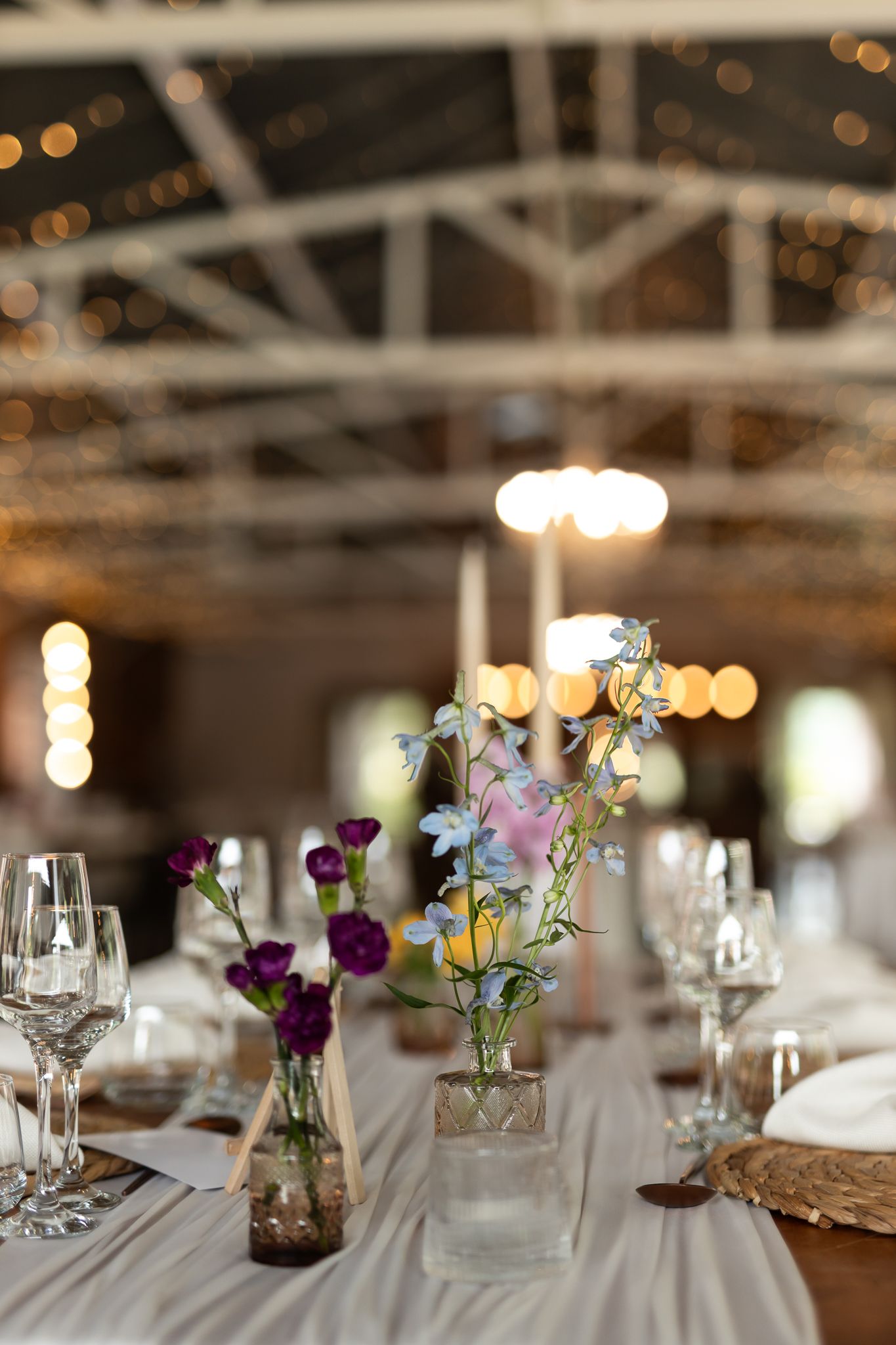 Elegant wedding reception table setting with delicate floral centerpieces and twinkling lights overhead.