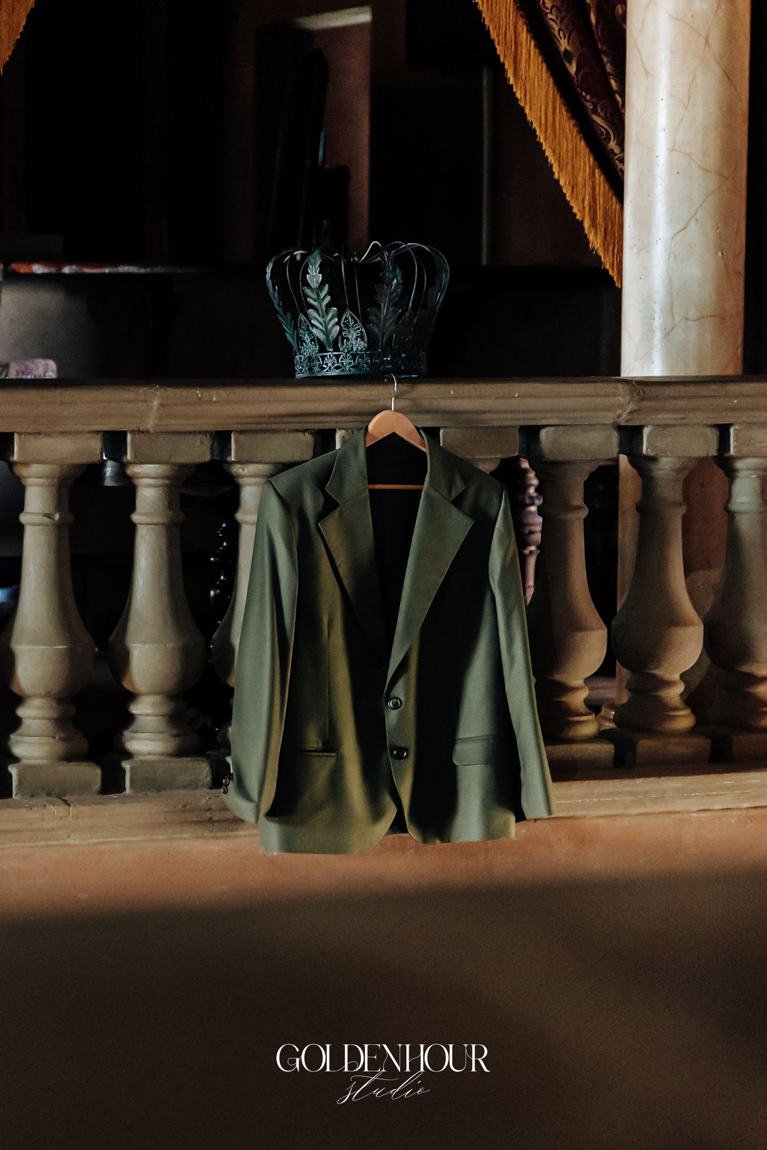 Green blazer on hanger with decorative crown at elegant wedding venue balcony.