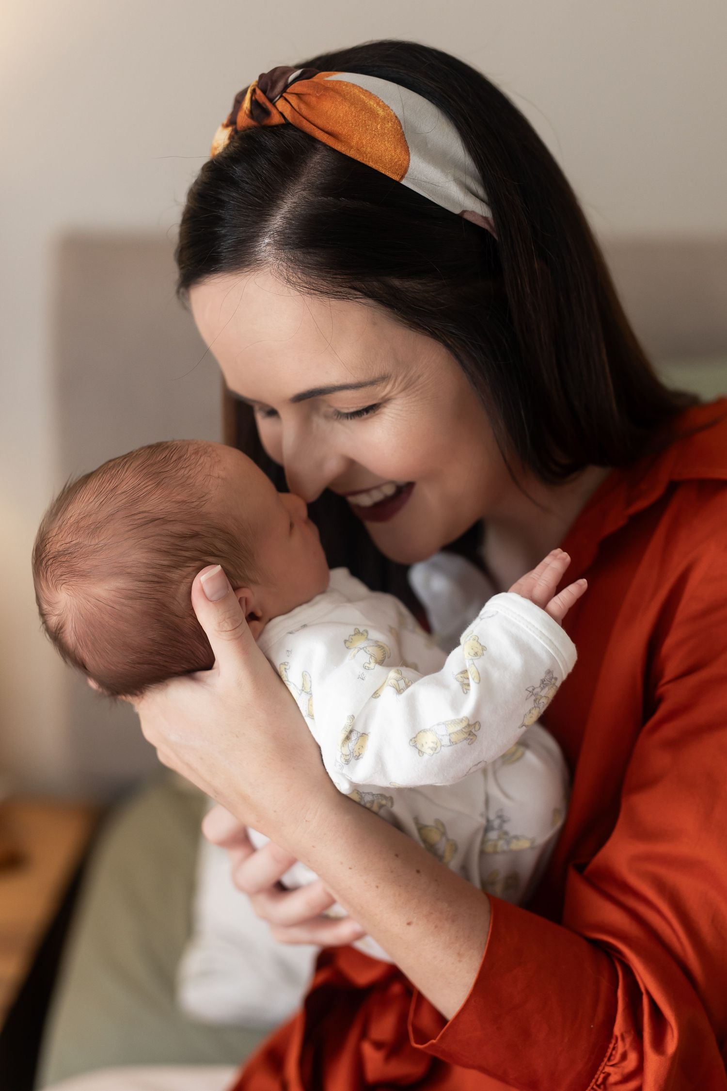 Parent wearing red sweater holding and snuggling with a small baby dressed in white.