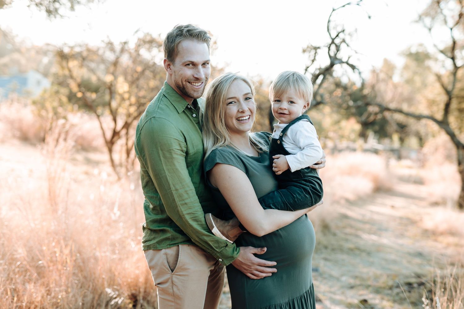 Family group dressed in green and neutral tones embracing outdoors during a golden hour photoshoot.