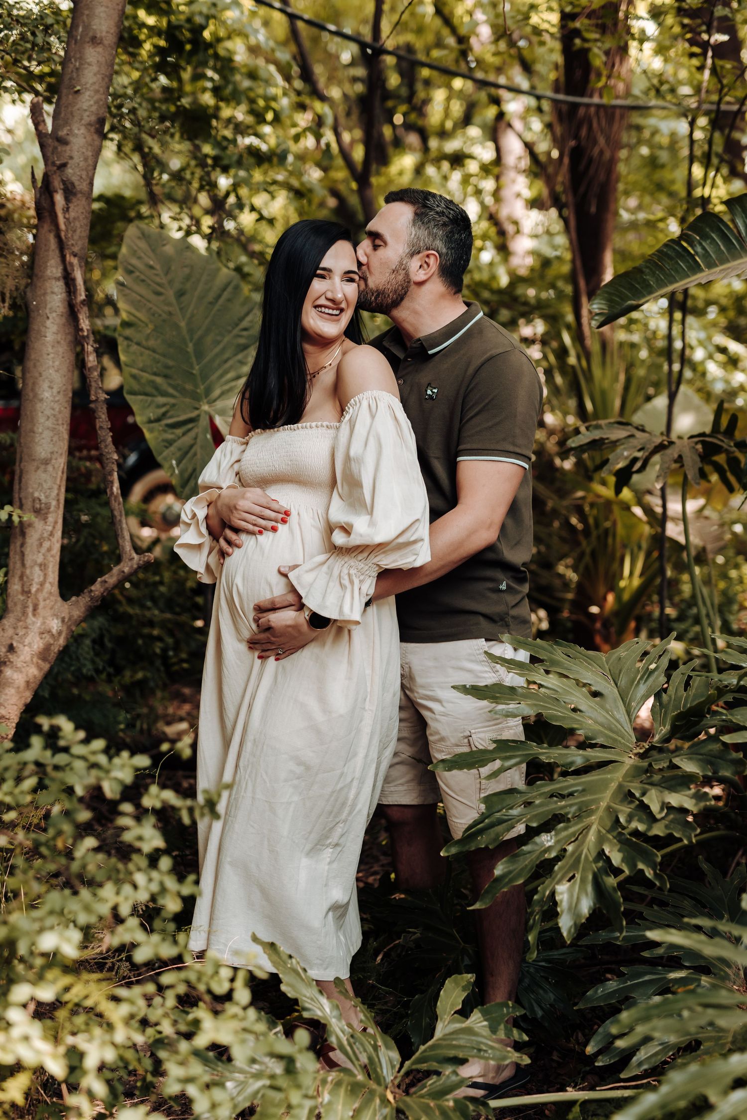 Romantic couple shares intimate moments while embracing in a lush garden setting filled with tropical plants and trees.