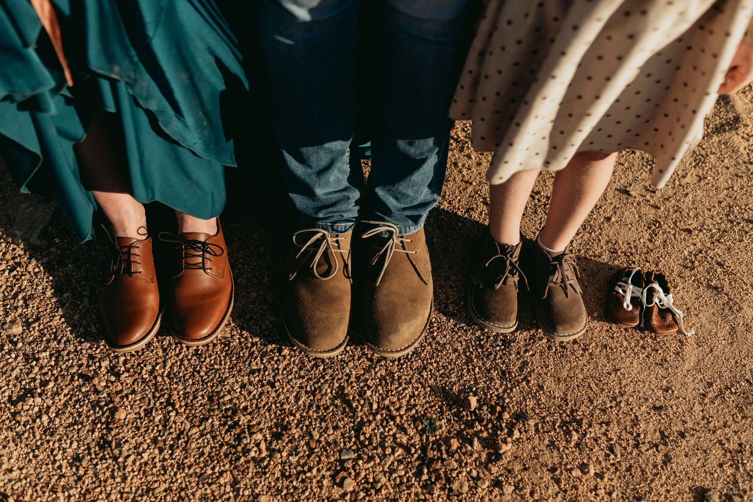 Close-up view of feet arranged in a row showing boots and shoes on desert ground.