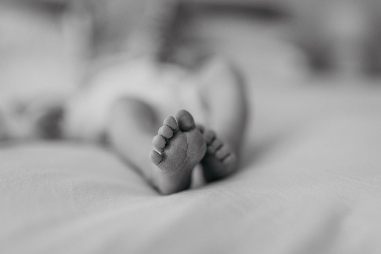 Black and white photograph showing delicate infant feet resting on white blanket.