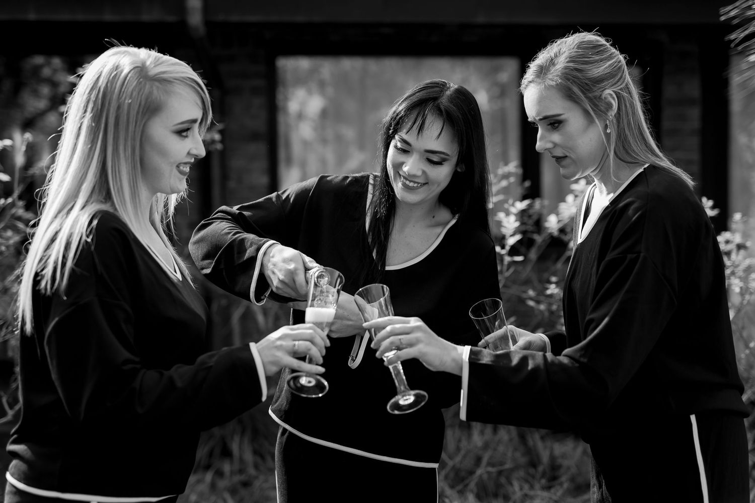 Group of women in black attire enjoying drinks and conversation at an outdoor gathering.