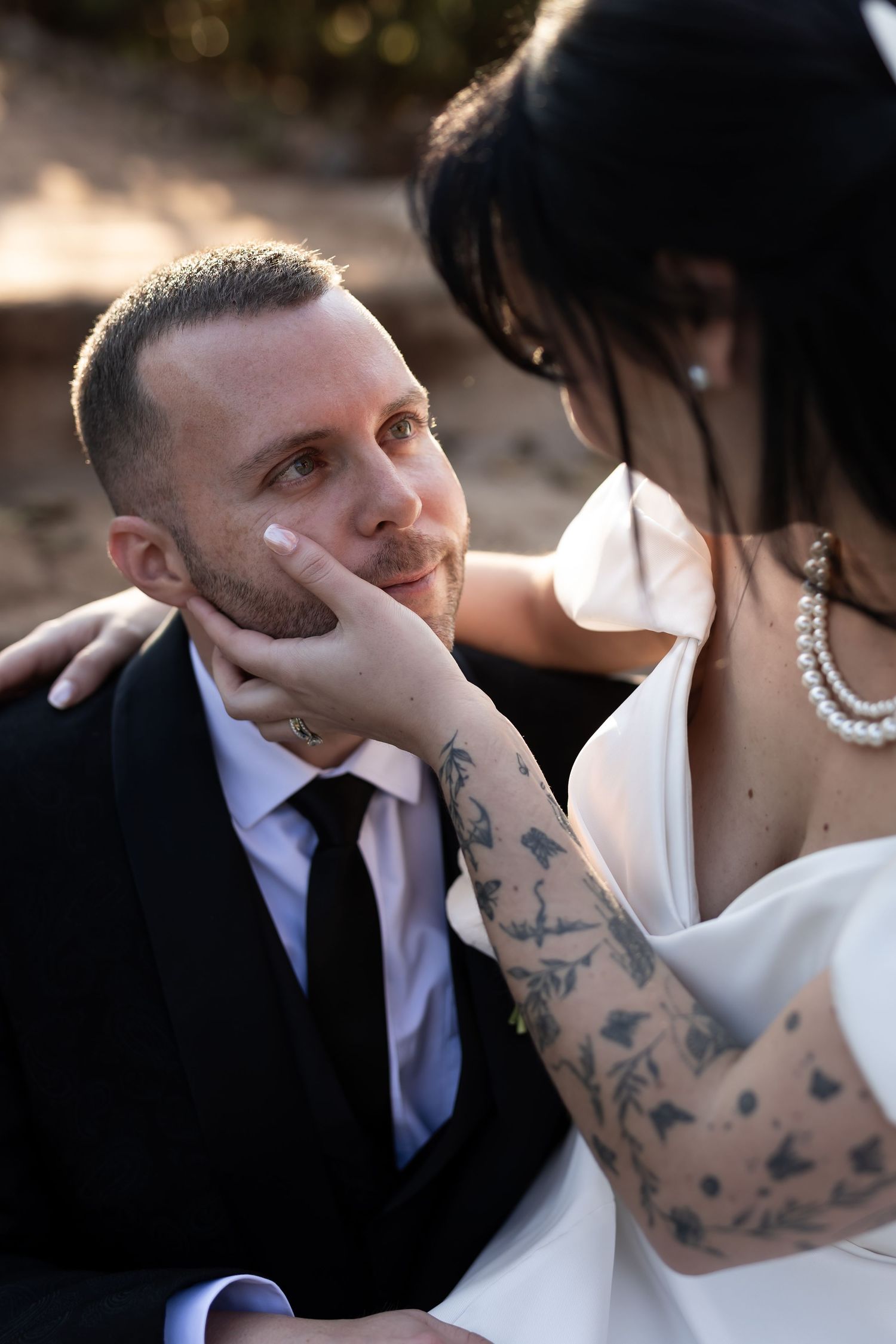 A tender wedding moment between a couple in formal attire as the bride gently touches her partner's face.