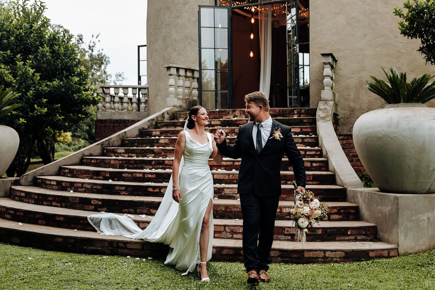 A couple shares romantic moments on outdoor stone steps surrounded by lush garden landscaping.