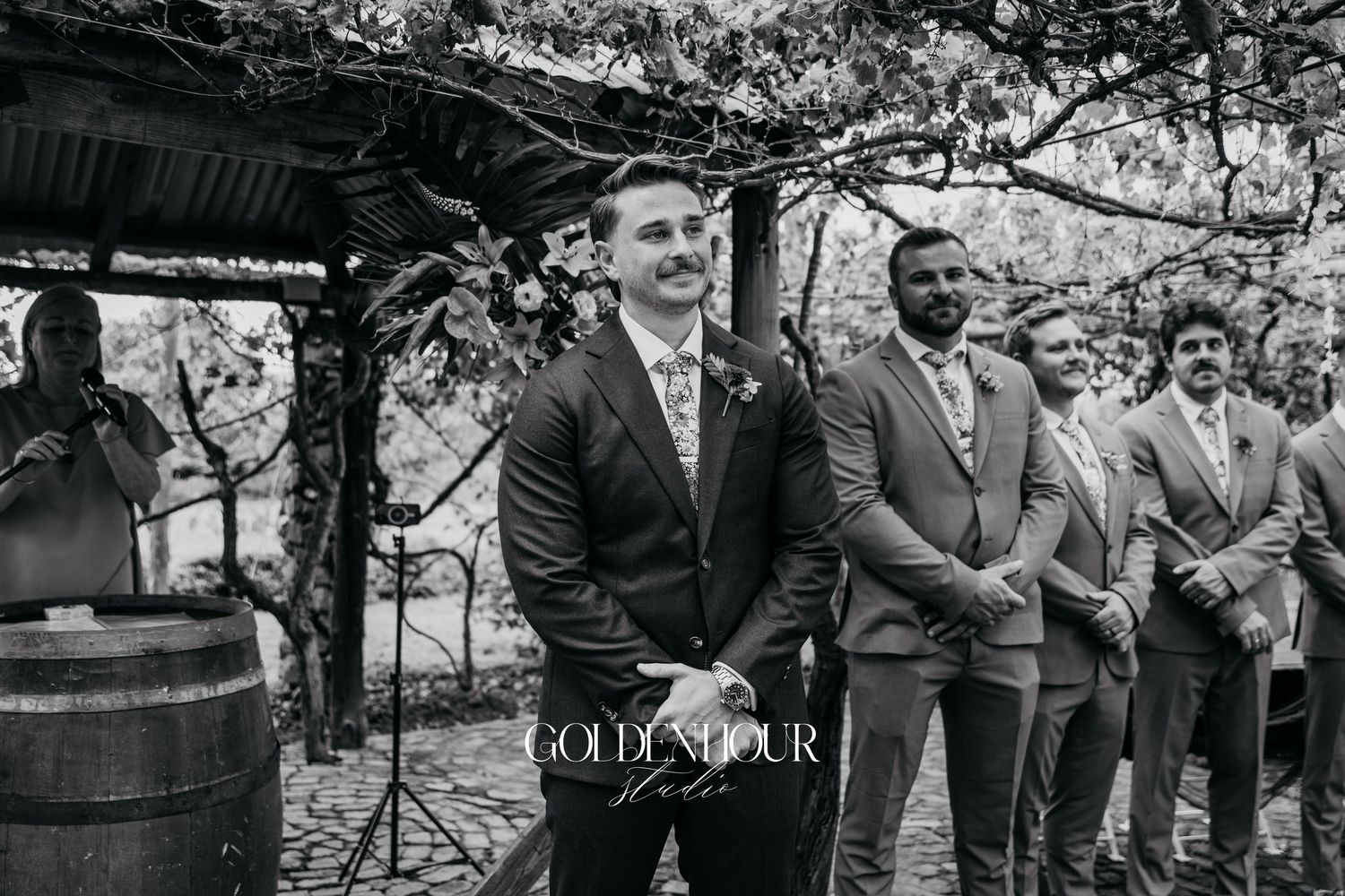 Wedding ceremony guests gathered outdoors under blooming trees in black and white.