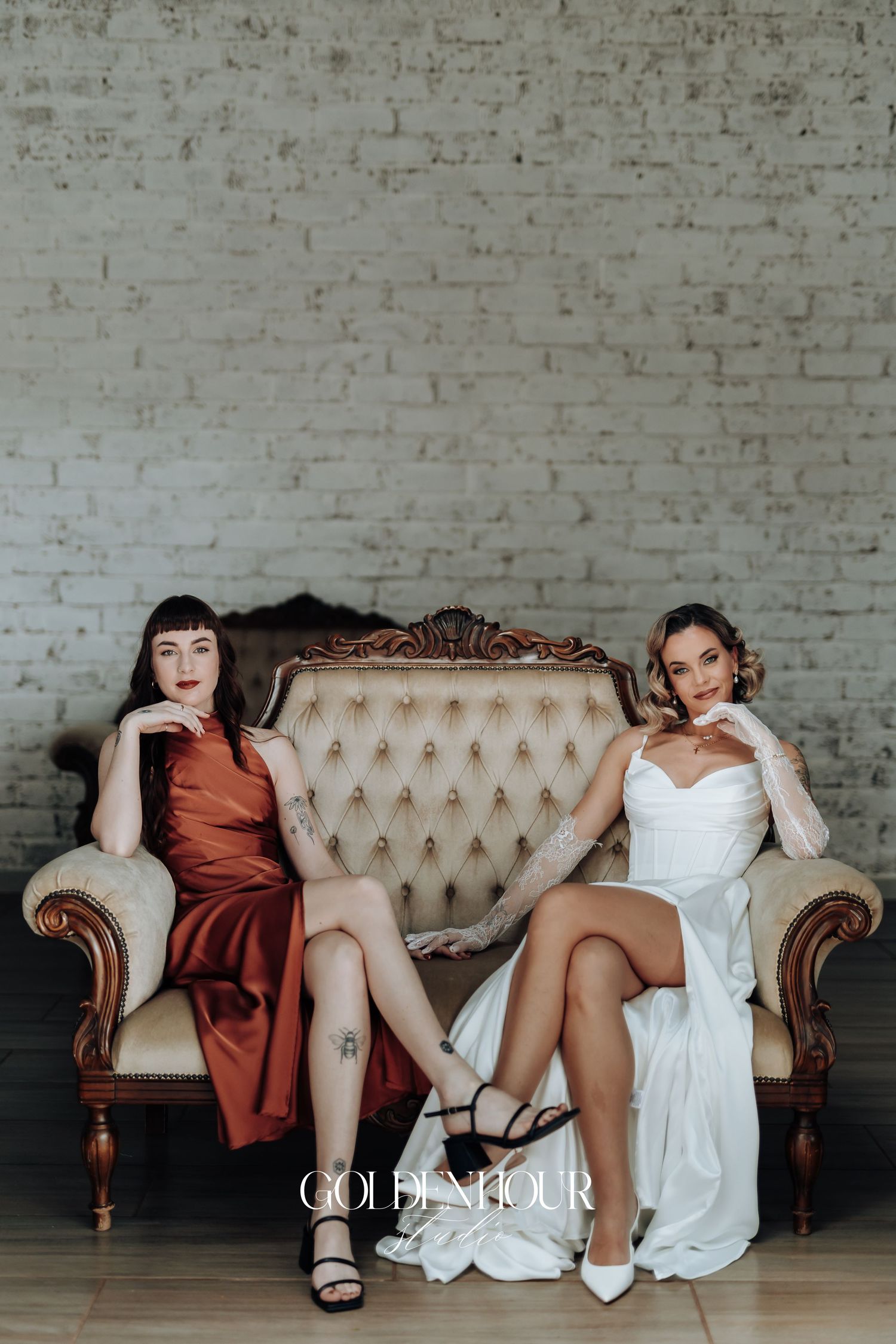 Wedding party lounging casually on an elegant beige tufted sofa in front of white brick wall.