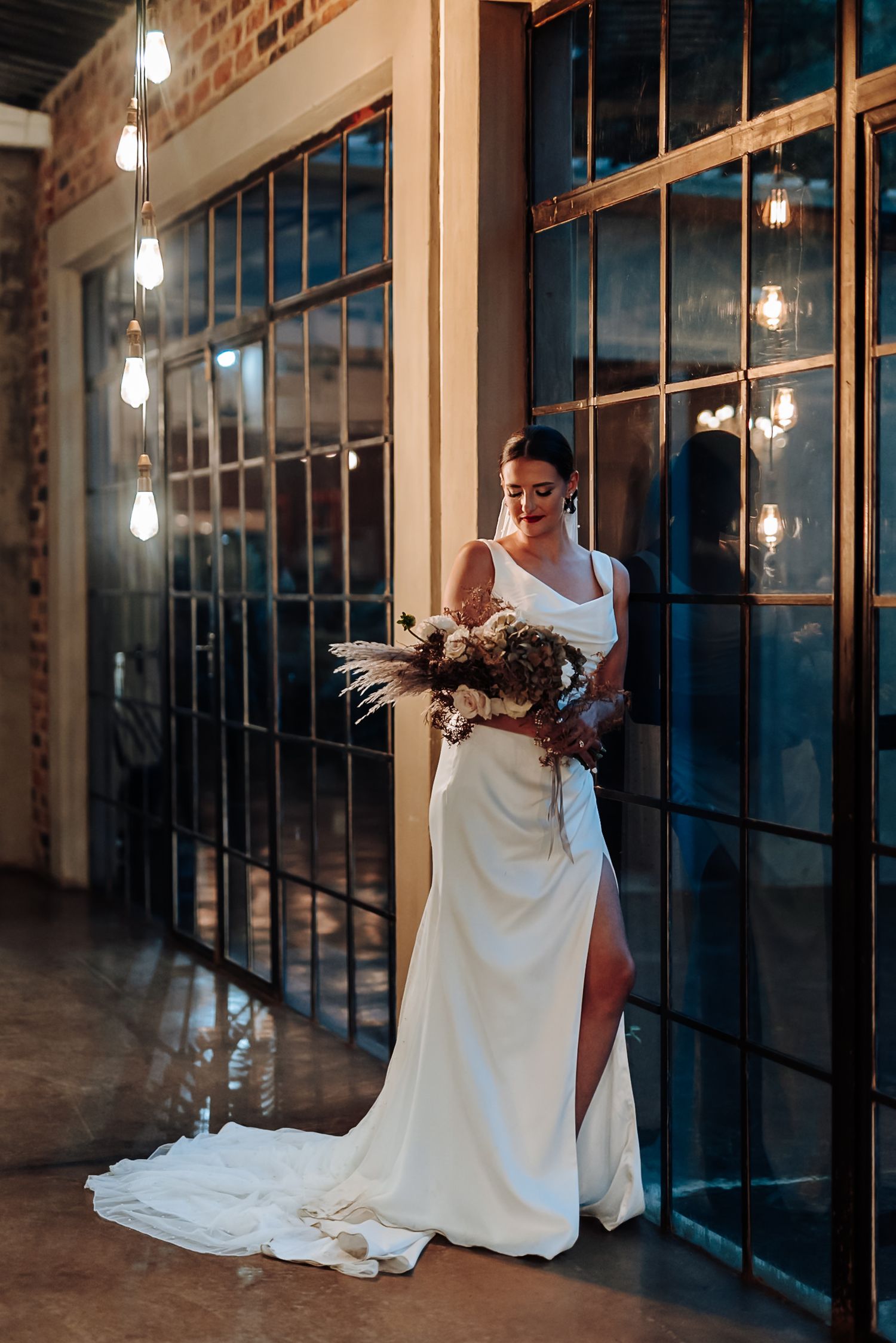A person in a flowing white dress sits on industrial steps in a brick-walled space with hanging pendant lights.