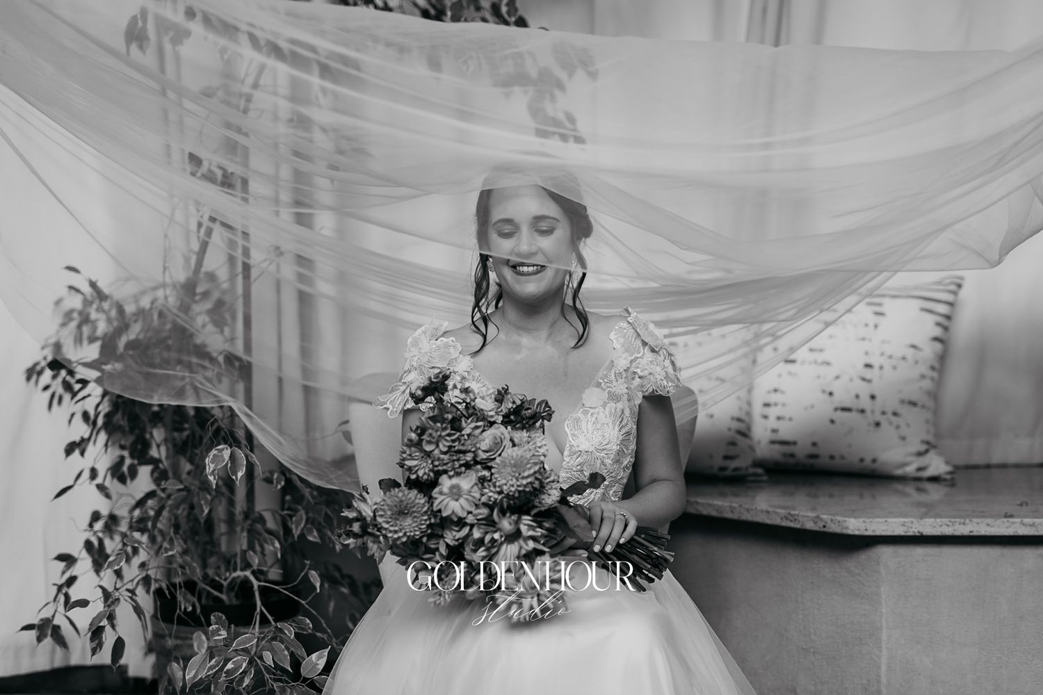 Bride in white gown holds floral bouquet as veil billows around her in a dreamy black and white wedding portrait.