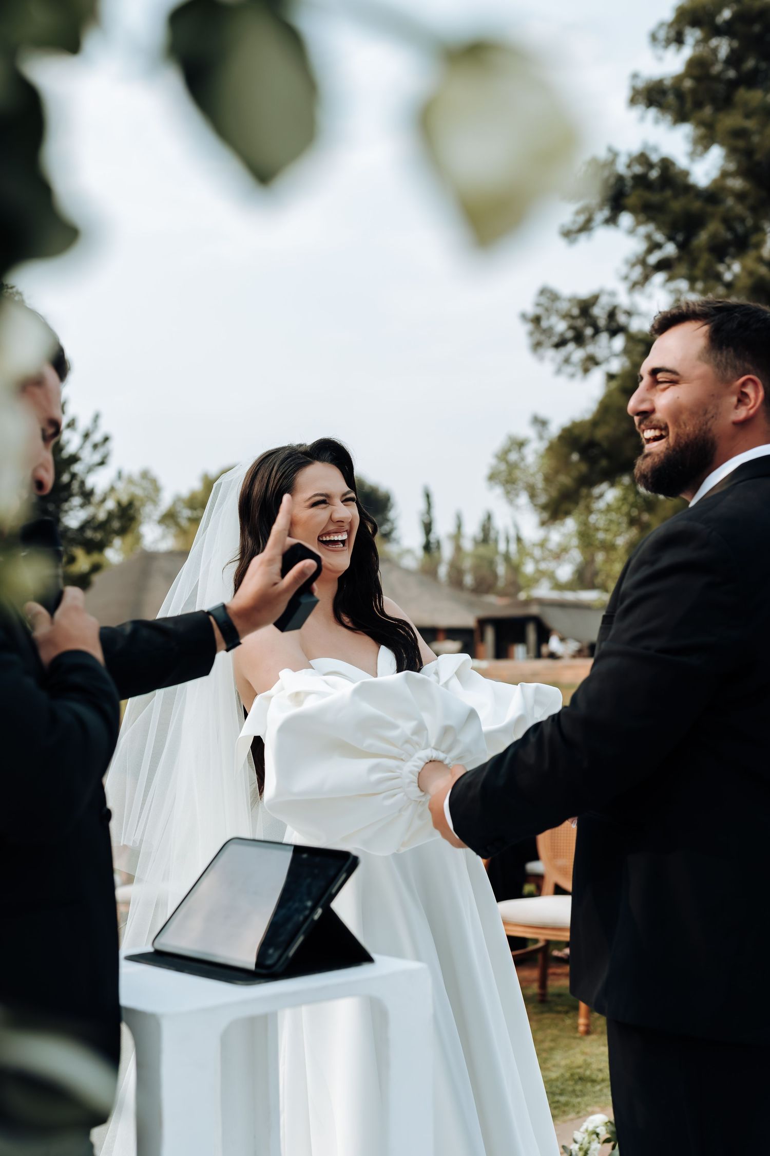 A couple shares a joyful moment during their wedding ceremony, with the bride wearing white and groom in black.