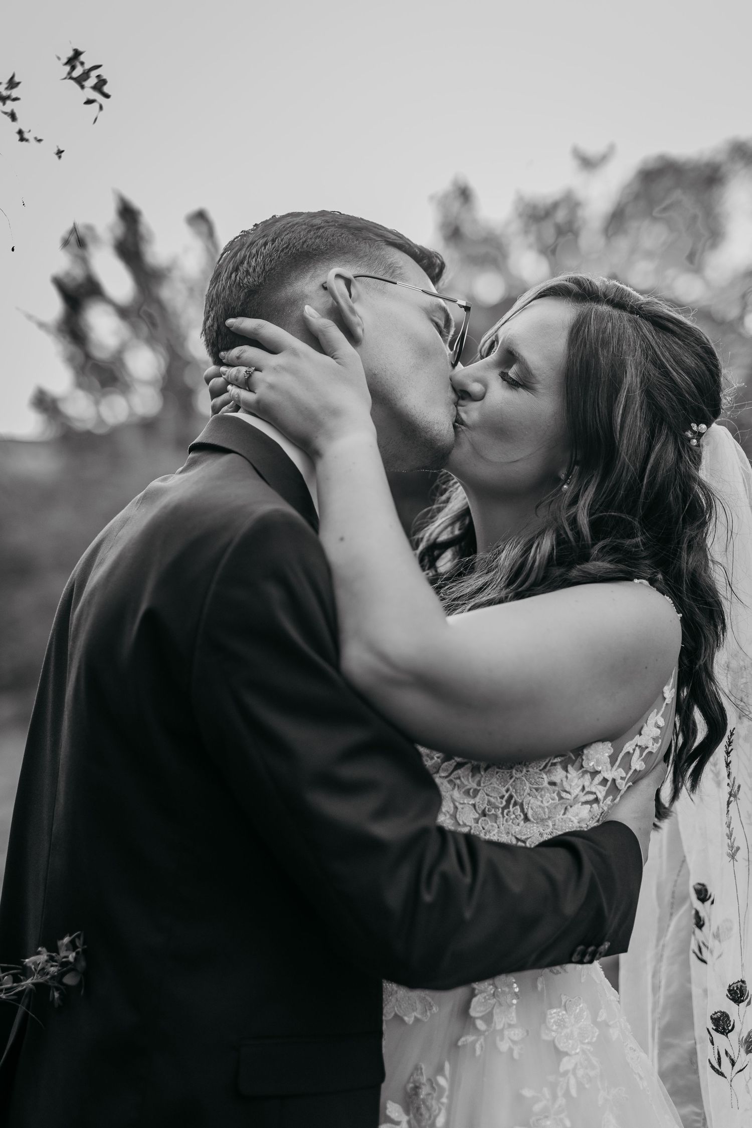 A romantic black and white wedding photo showing a passionate kiss between a couple outdoors.
