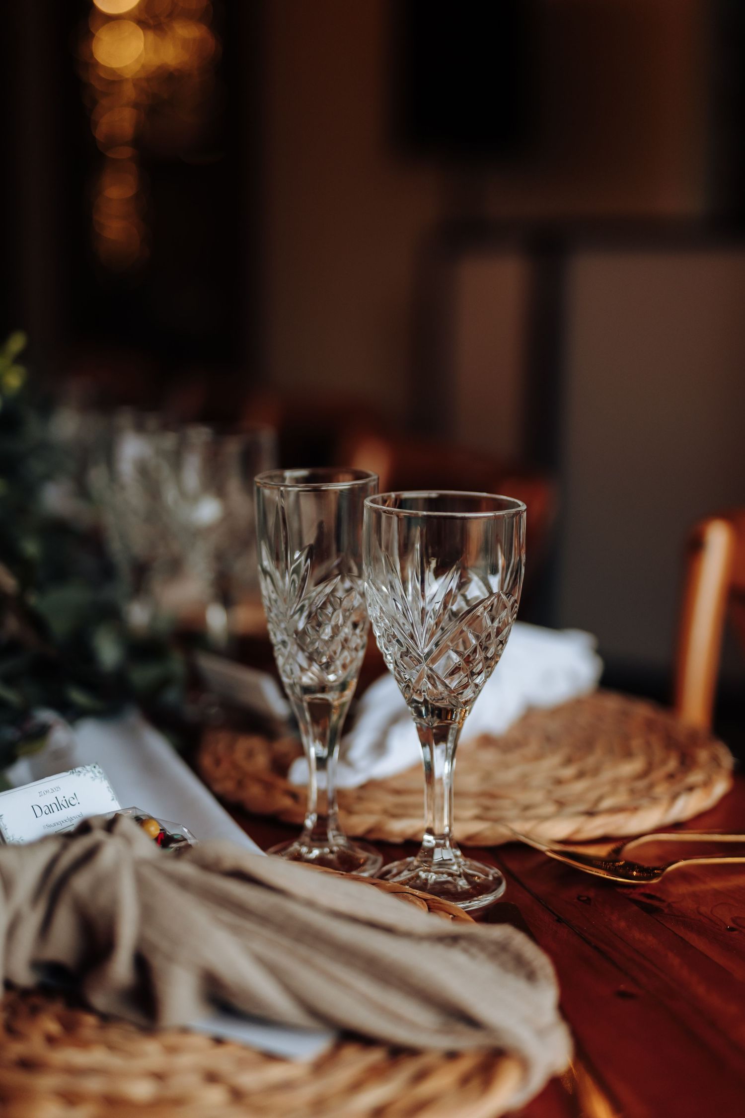 Crystal wine glasses and place settings arranged on an elegant table with soft mood lighting and neutral linens.