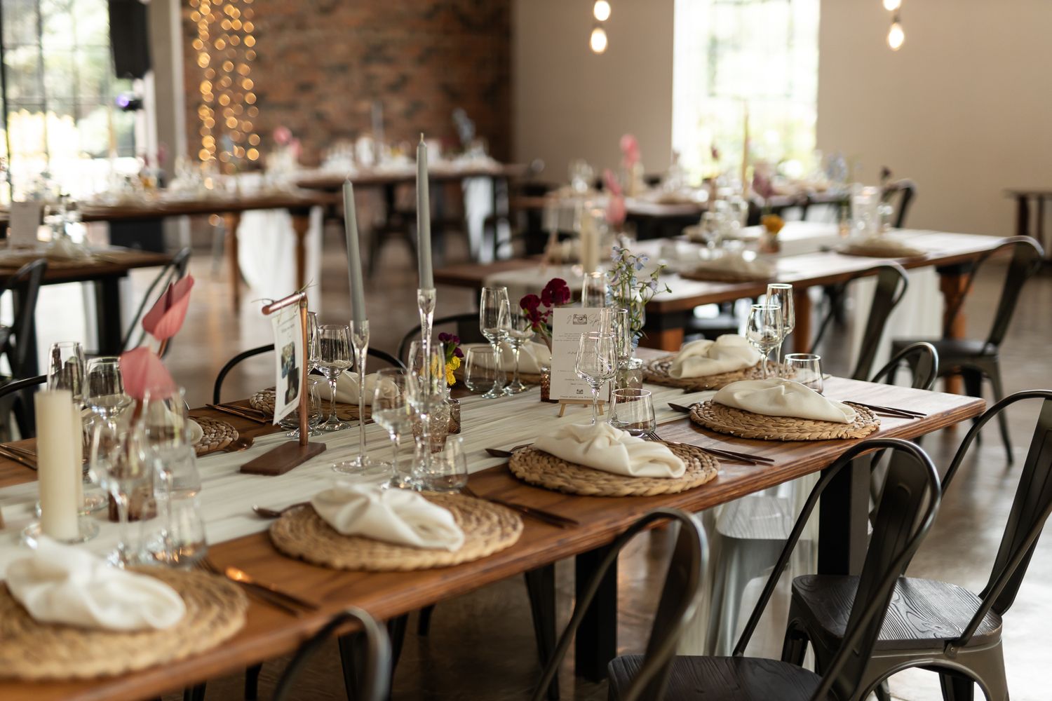 Rustic wedding reception table setting with wooden tables, metal chairs and elegant place settings.