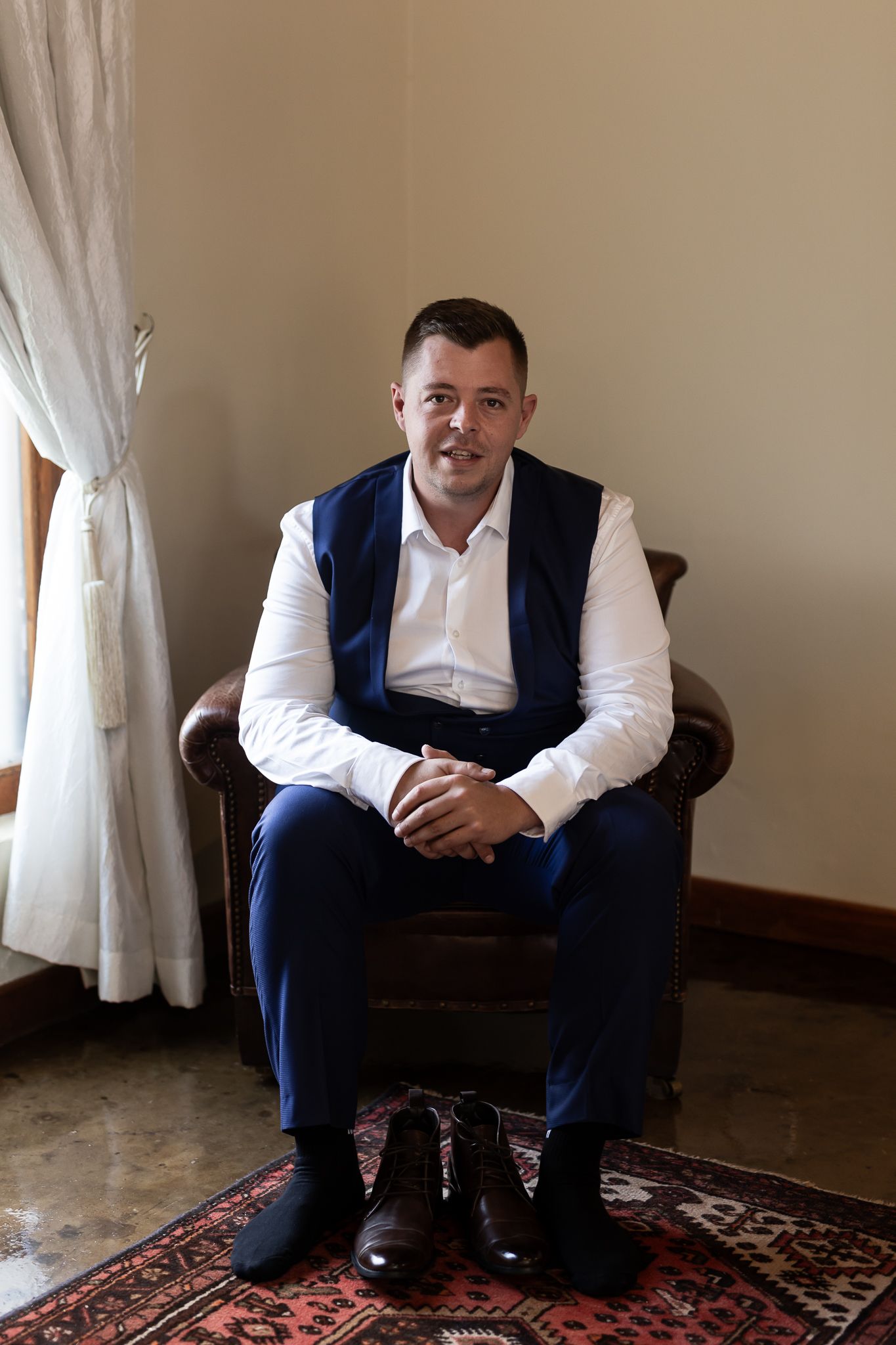 A formal portrait in a room with a man wearing a navy vest and white shirt.