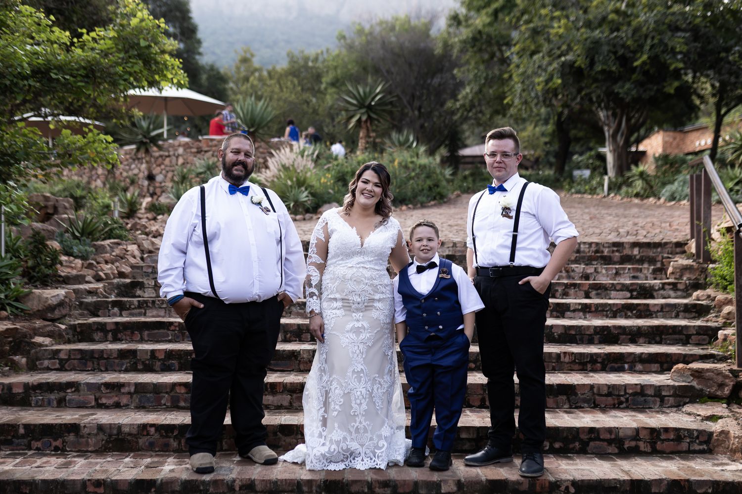 Small wedding party poses together on stone steps at outdoor venue.