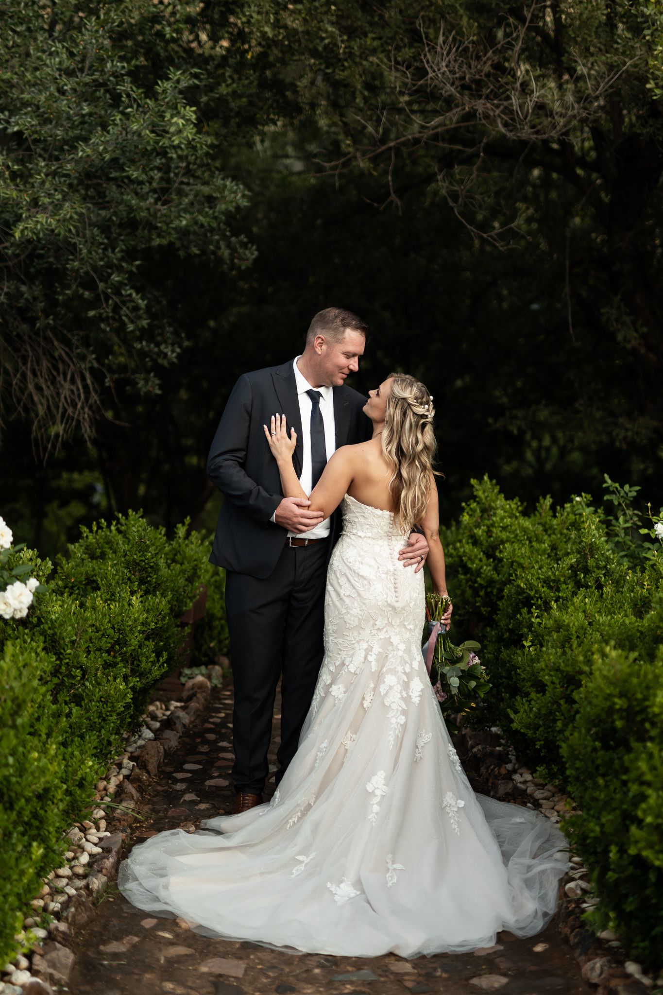 Elegant wedding portrait on a stone path surrounded by manicured shrubs.