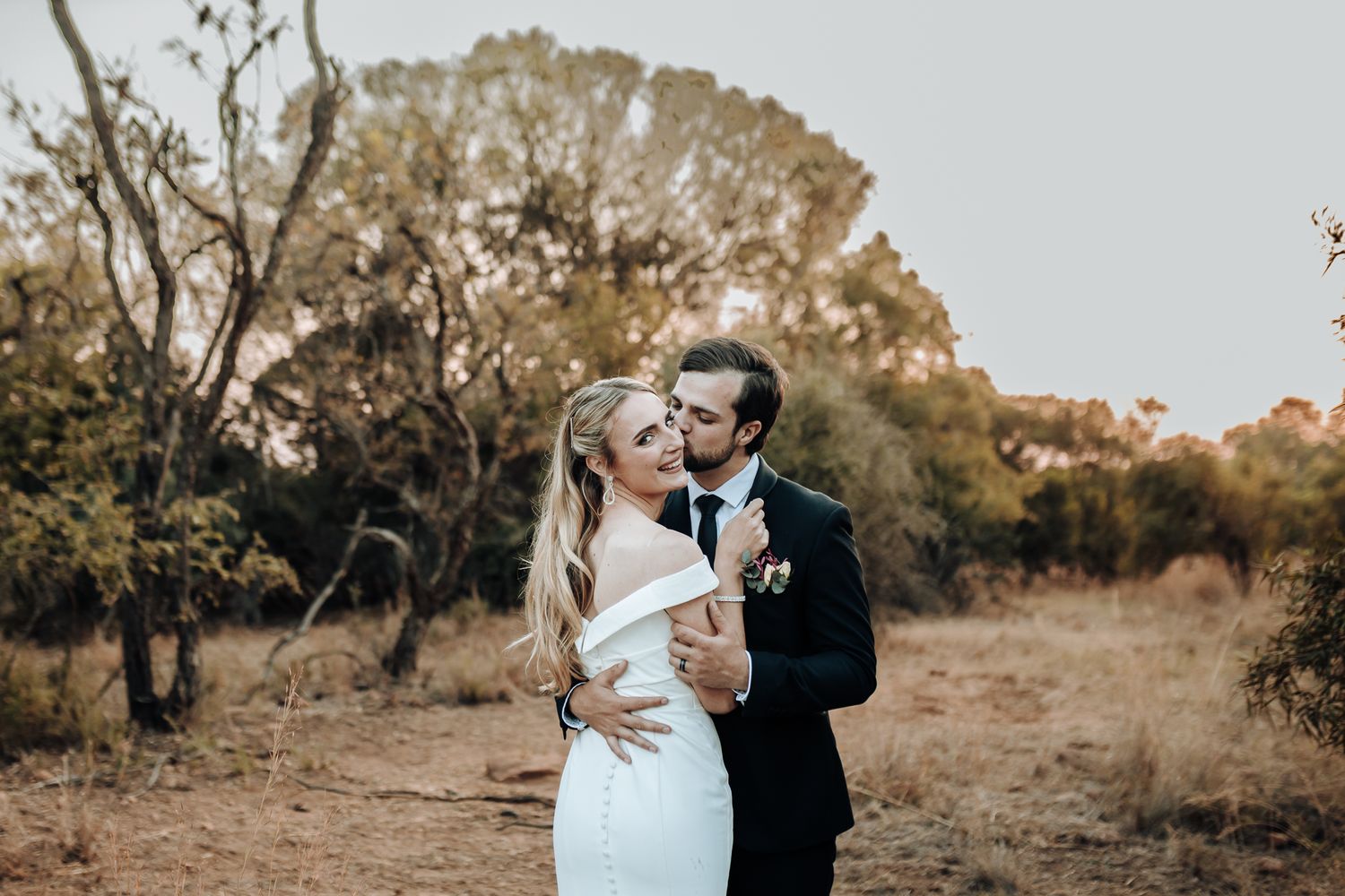 A couple shares a romantic moment among trees in an outdoor setting.