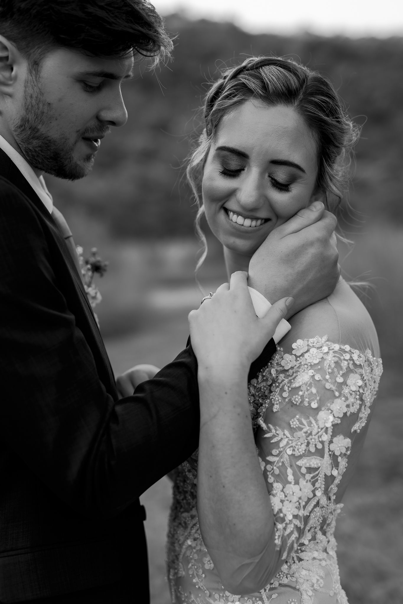 An intimate black and white portrait of newlyweds sharing a tender moment outdoors.