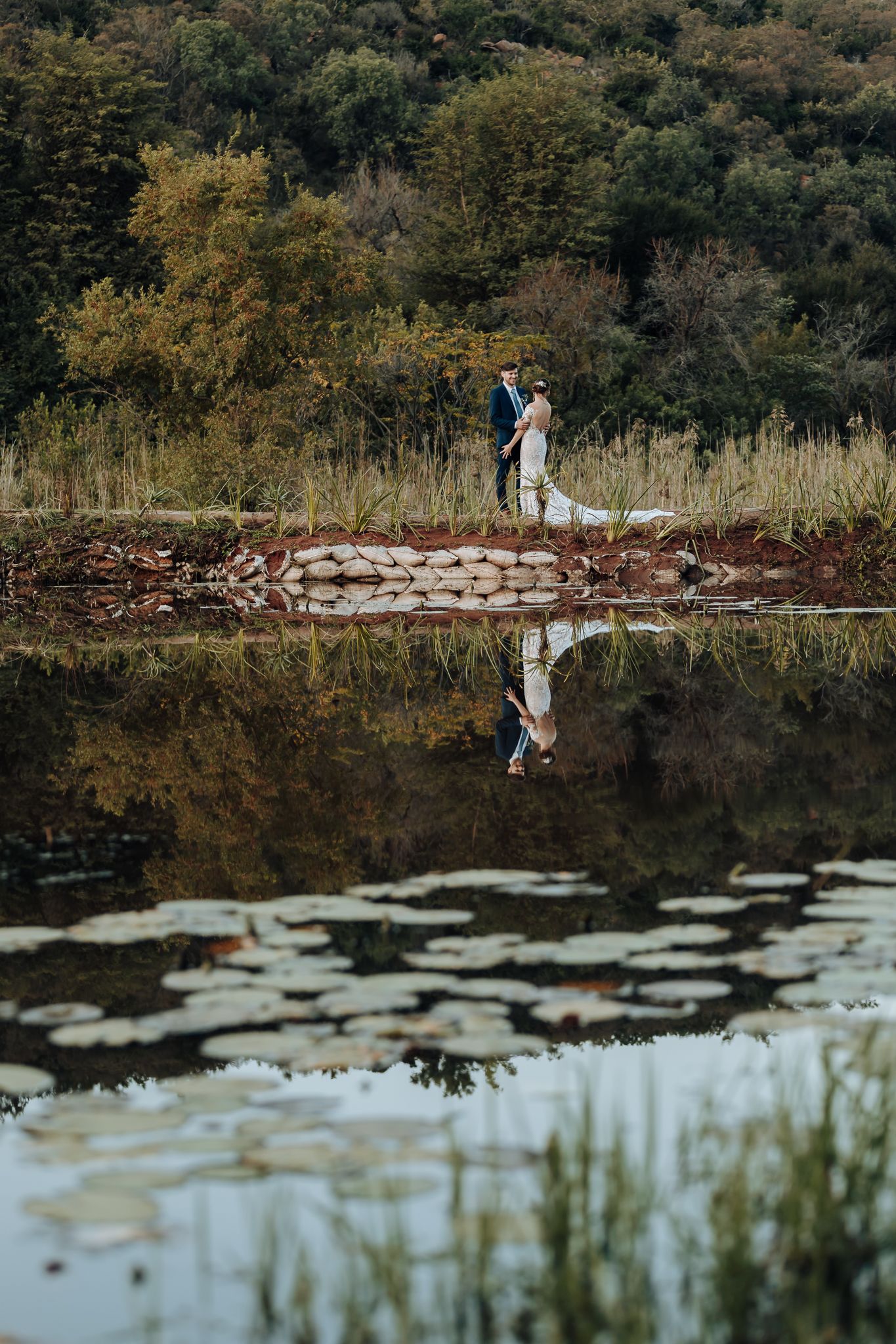 Artistic wedding photo with reflection in still water against mountainous autumn landscape.