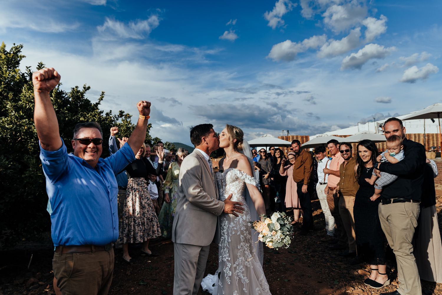 Wedding celebration with guests cheering during an outdoor ceremony.