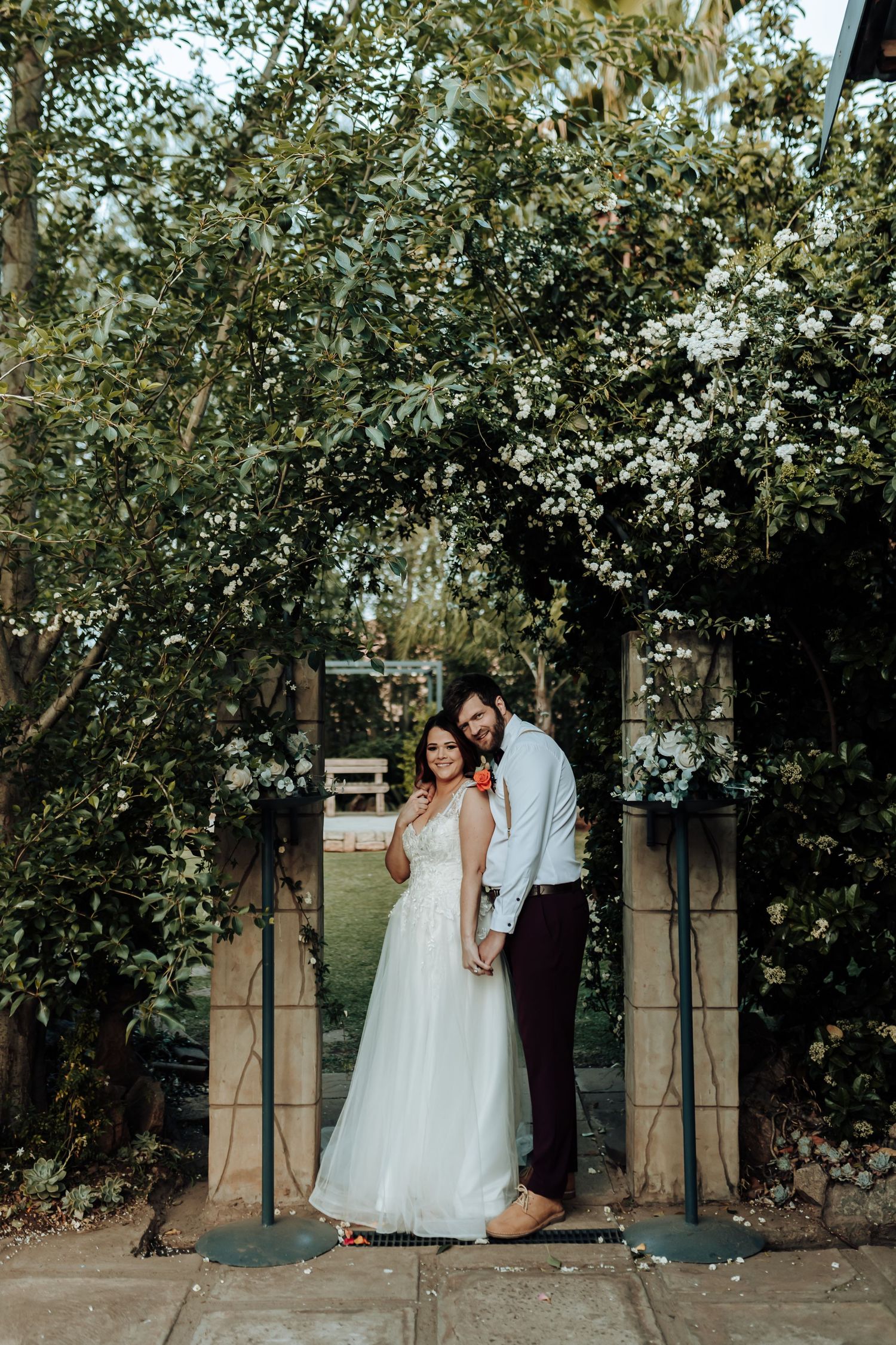 Couple posing under blooming garden archway in outdoor wedding setting.