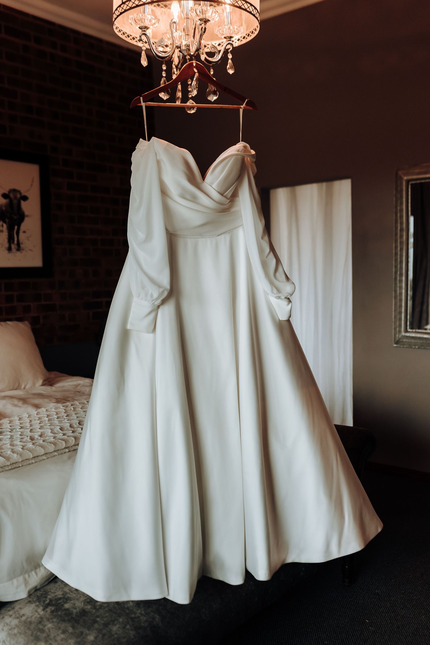 An elegant white wedding dress with sweetheart neckline hanging from a crystal chandelier.