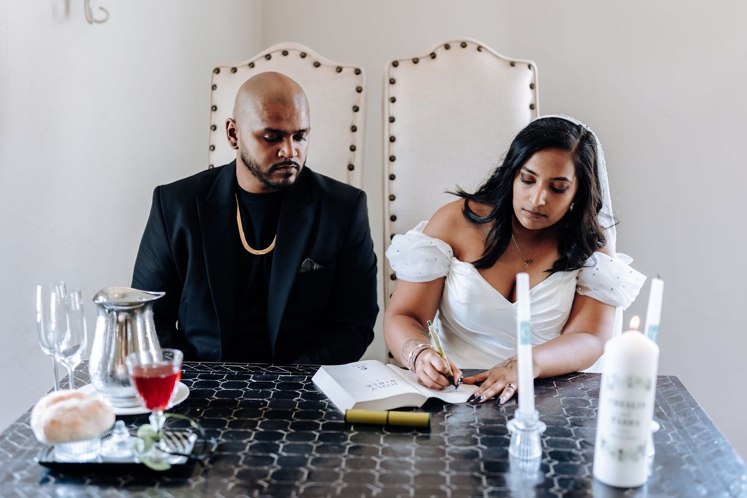 Newlyweds sitting at reception table with wine glasses and place settings.