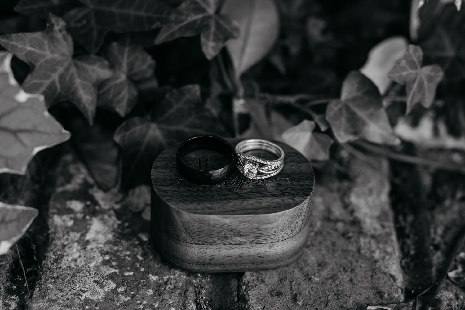 Wedding ring placed on wooden surface surrounded by dark leaves.