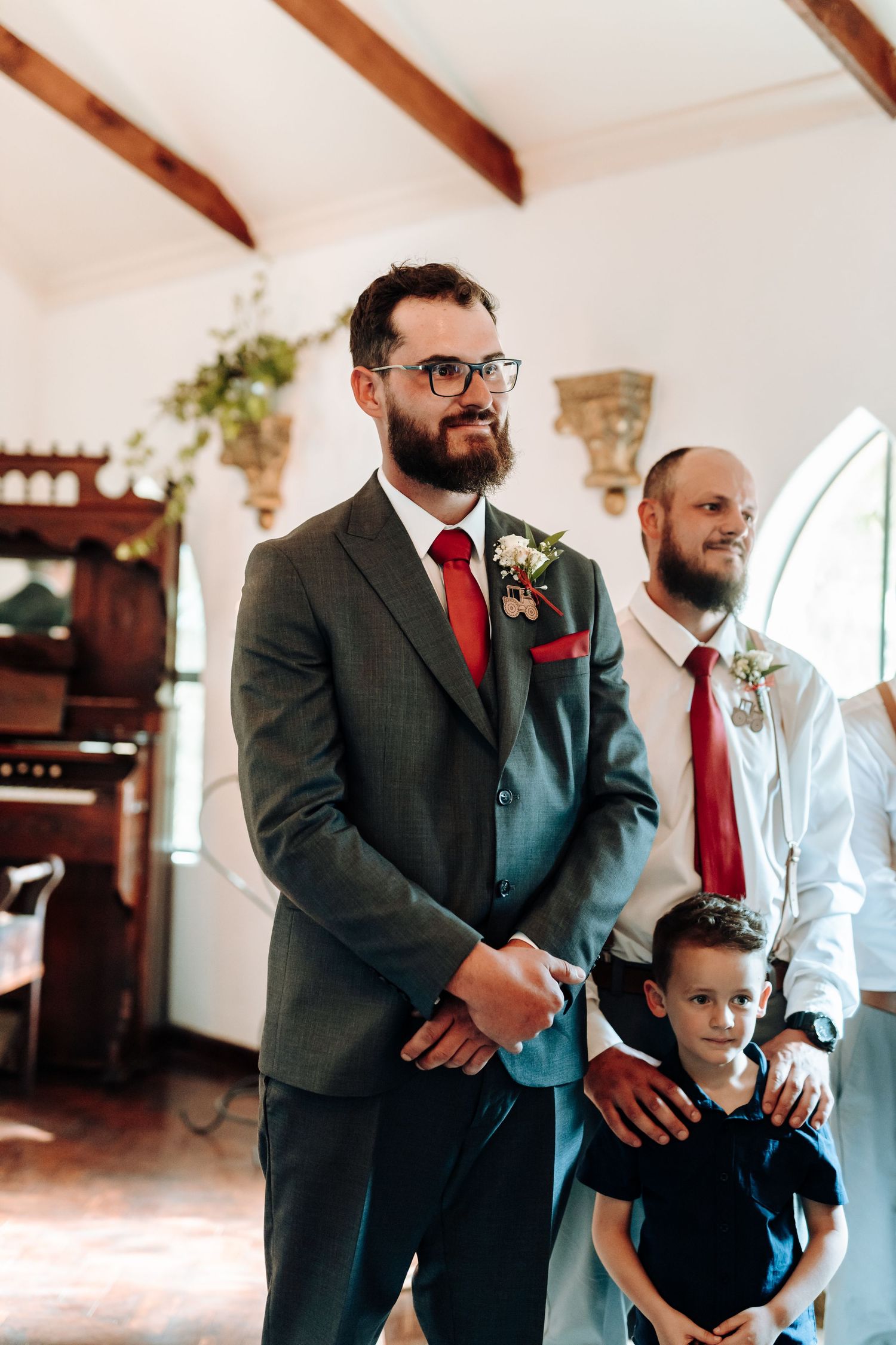 Wedding party members in formal attire standing at altar in chapel with exposed wooden beams.