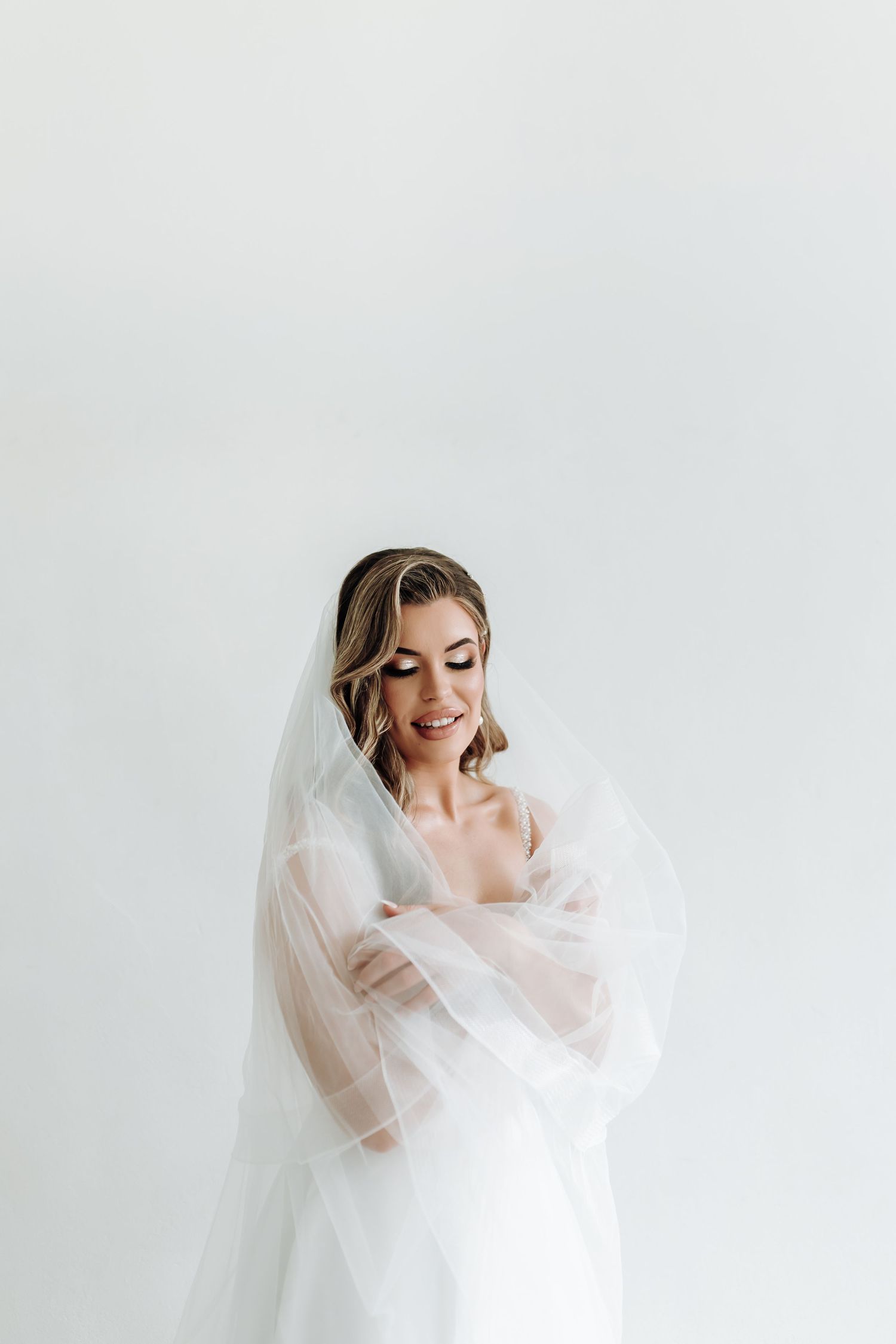 Ethereal bridal portrait against white backdrop featuring delicate veil and sheer sleeves.