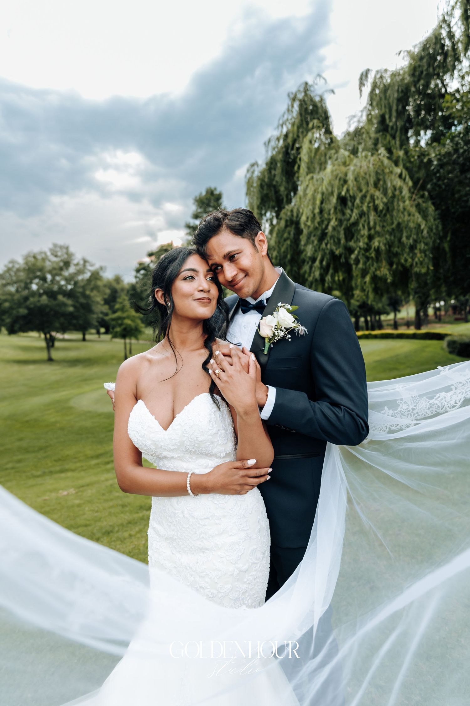 Romantic wedding portrait with flowing veil against scenic willow trees and golf course background.