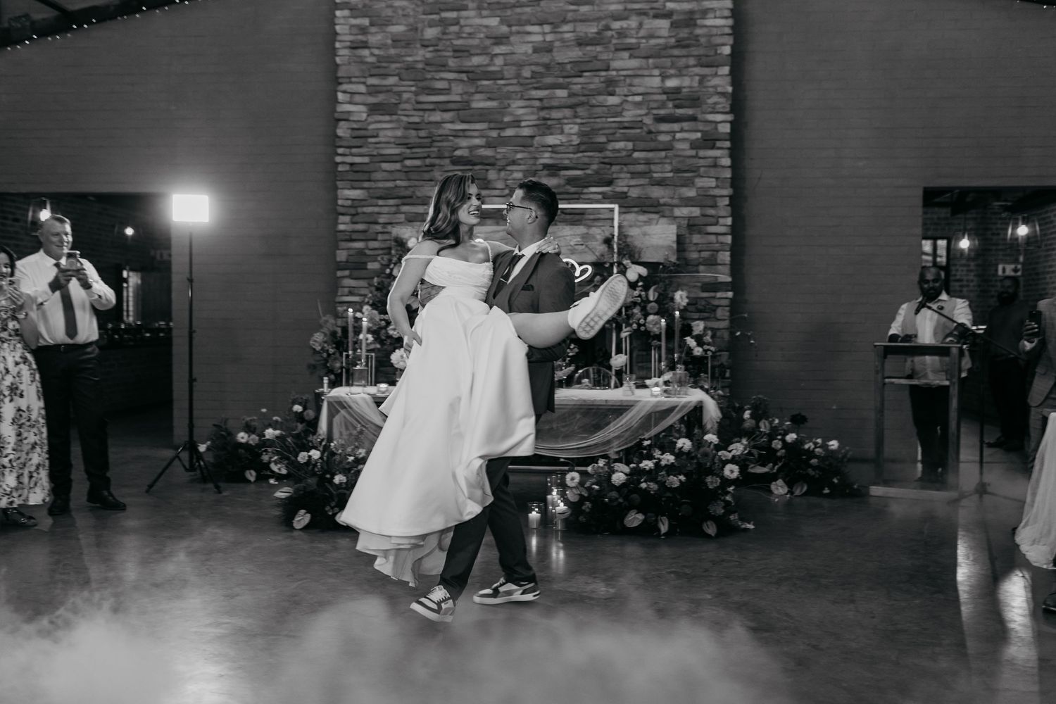 Wedding guests dancing in a dimly lit reception hall with brick accent walls.