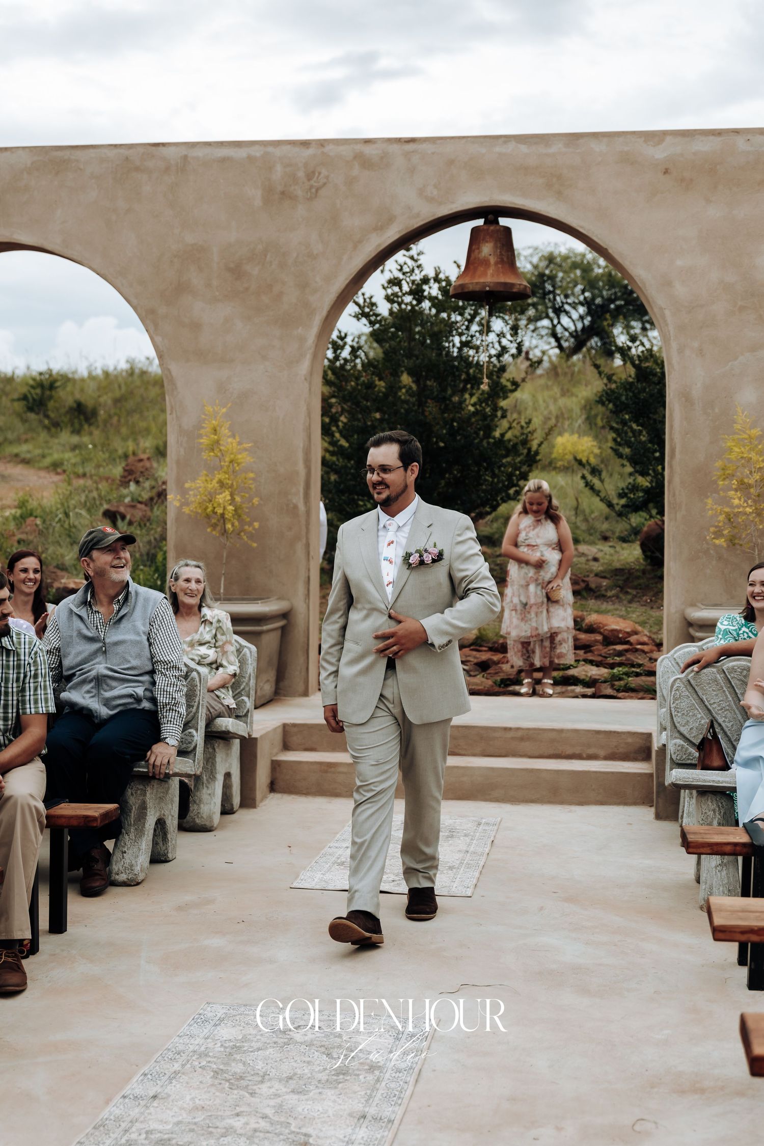 Wedding ceremony at outdoor venue with stone arches and seated guests.